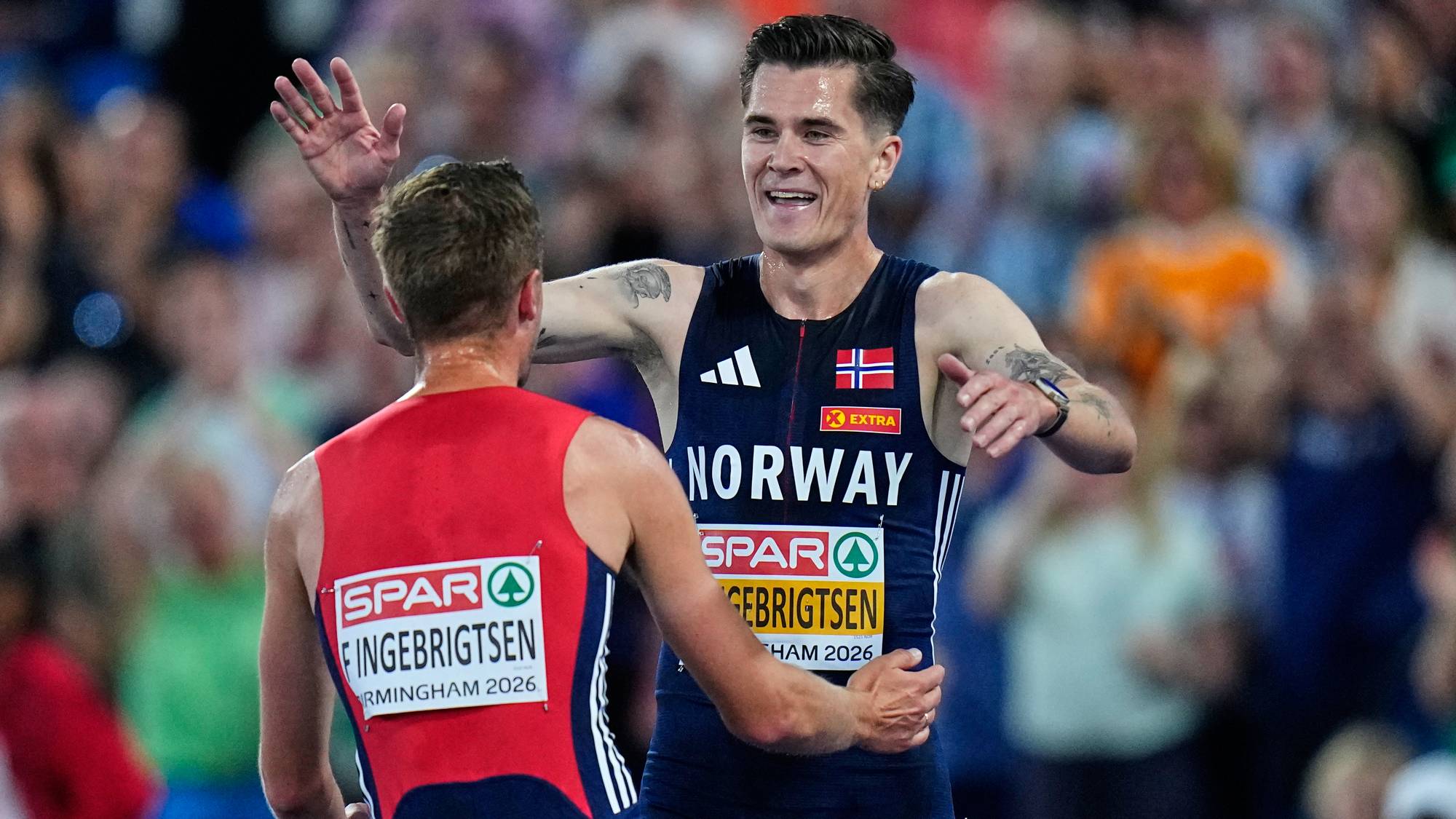 Jakob Ingebrigtsen feirer sammen med Filip Ingebrigtsen på løpebanen foran et publikum. (Bildebeskrivelsen er laget av en KI-tjeneste)