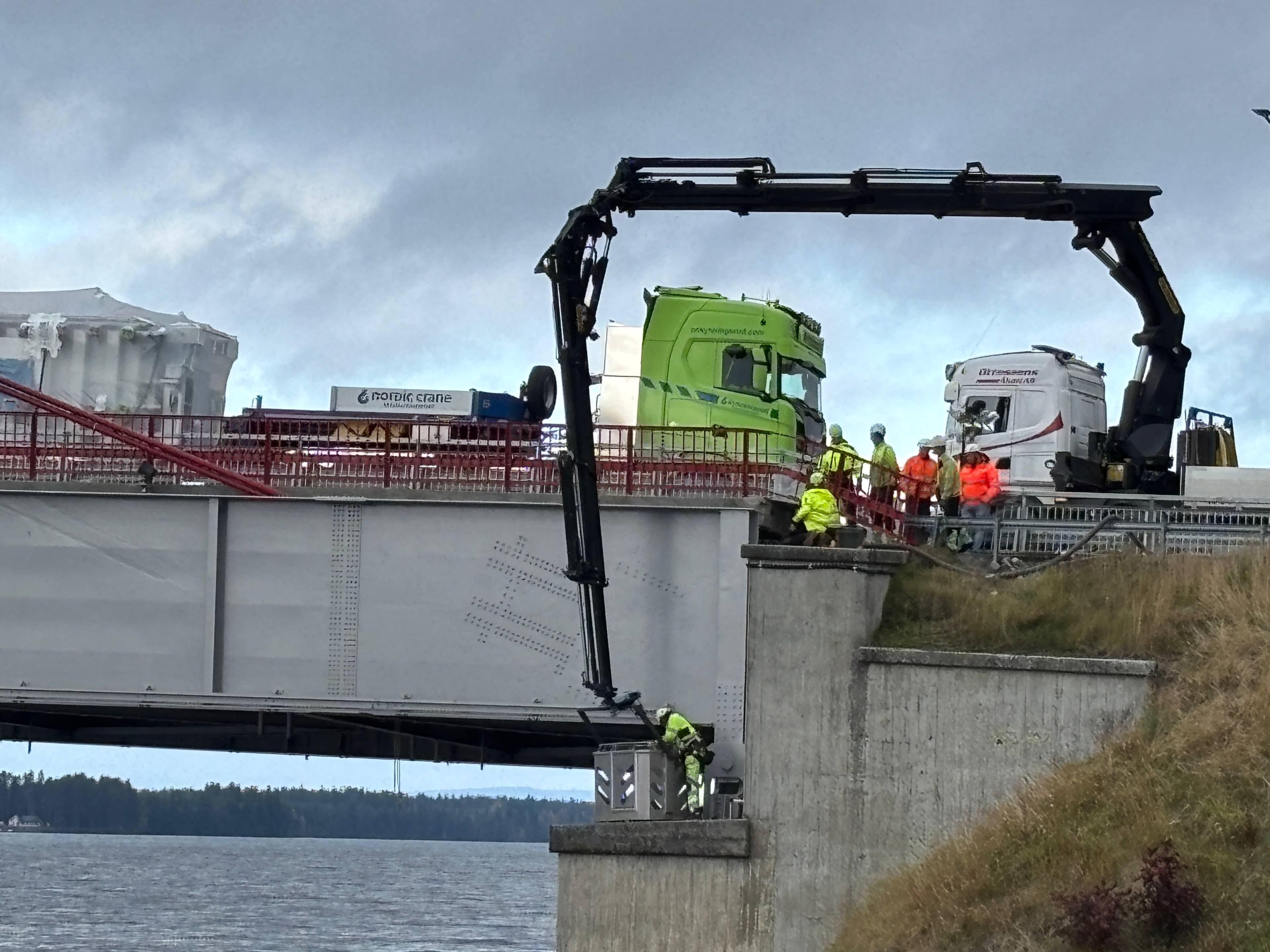 Kranbil utfører arbeid ved en bro med lastebiler stående på brodekket. Personell i arbeidsbekledning. (Bildebeskrivelsen er laget av en KI-tjeneste)