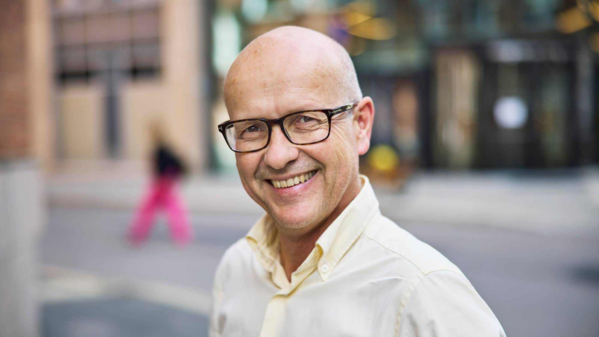 Professor i informatikk, Olav Lysne, en mann i 50-årene med mørk brilleinnfatning, uten hår, står i en bygate med kremhvit skjorte på seg.