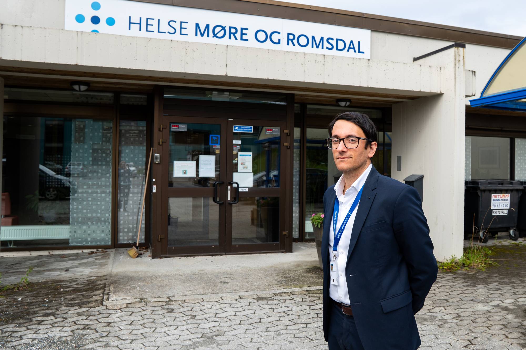 Ein mann med blå dressjakke og kvit skjorte. Han har svart hår og briller. 