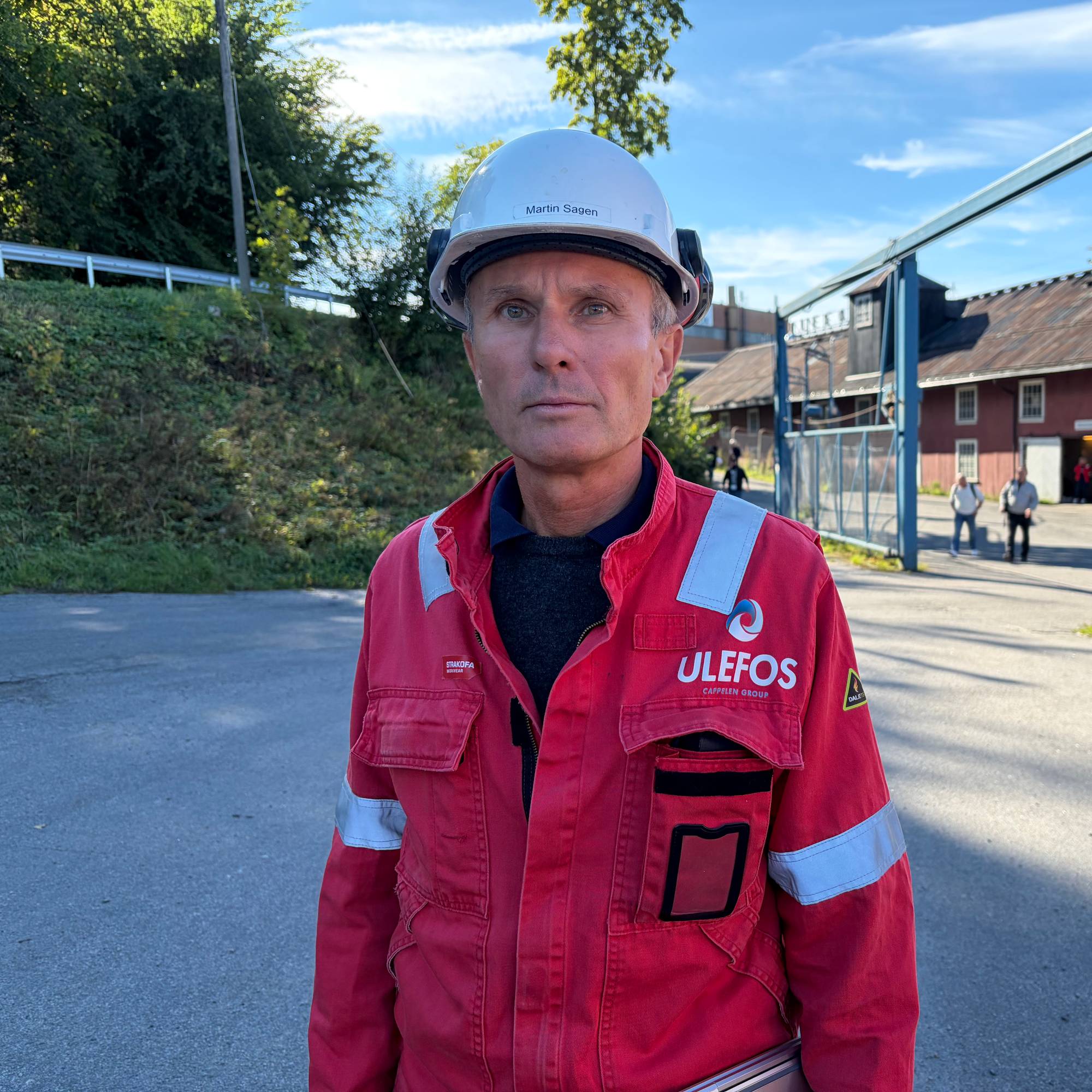 Martin Sagen med verneutstyr foran Ulefos Jernværk. Bakgrunnen viser industriområdet. (Bildebeskrivelsen er laget av en KI-tjeneste)