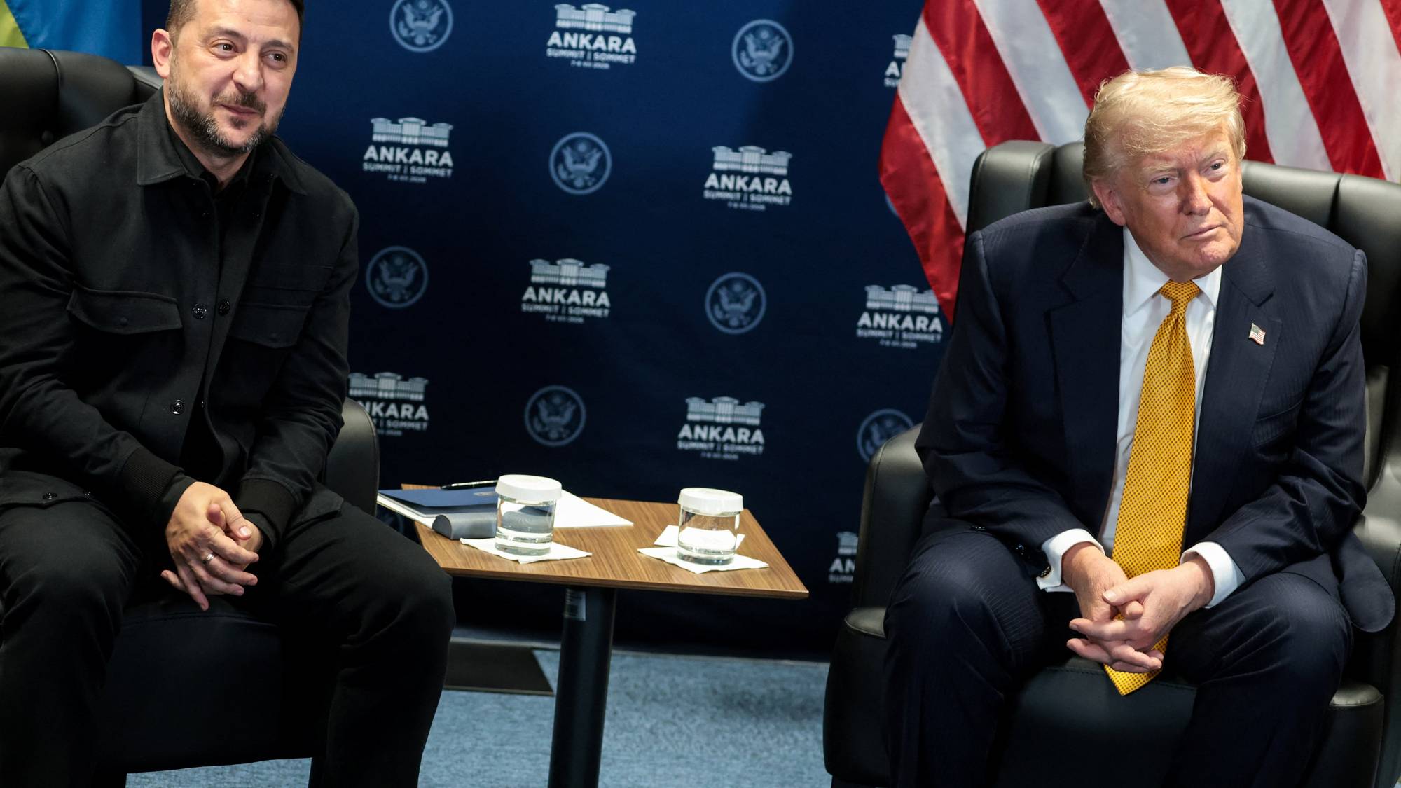 Volodymyr Zelenskyj og Donald Trump sitter i hver sin stol foran en bakvegg med logoer. Illustrasjon. (Bildebeskrivelsen er laget av en KI-tjeneste)