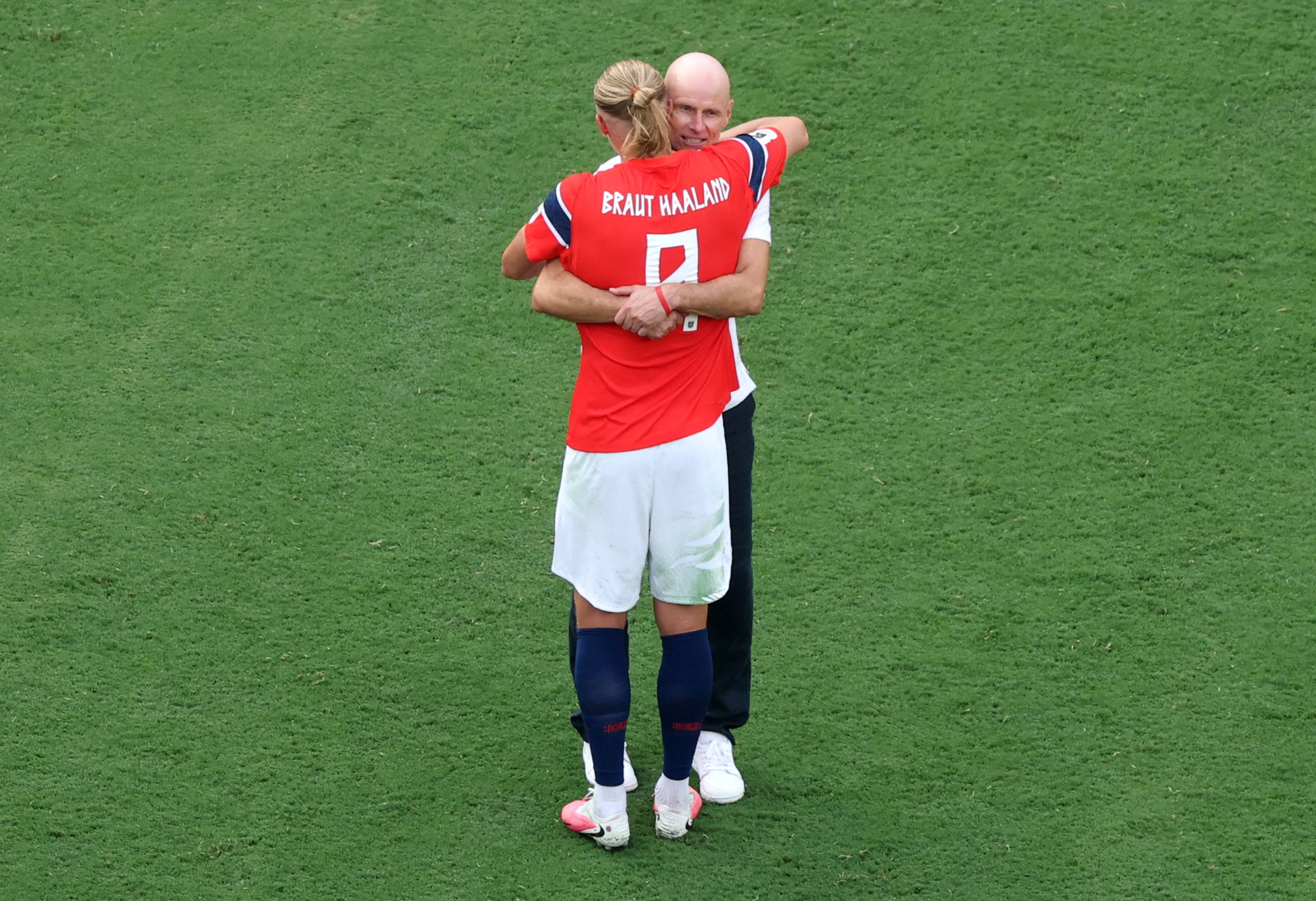 Erling Braut Haaland klemmer landslagstrener Ståle Solbakken på en fotballbane. (Bildebeskrivelsen er laget av en KI-tjeneste)