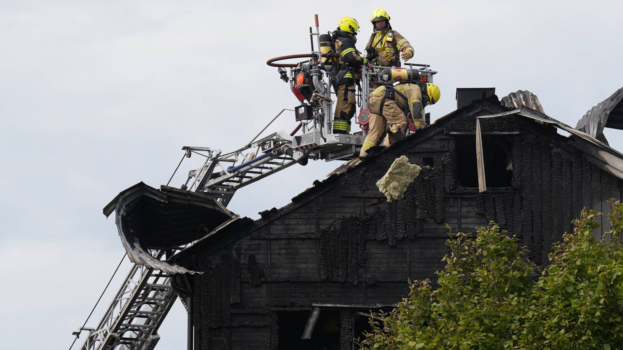 Brannvesenet arbeider på taket av et nedbrent hus etter brann. (Bildebeskrivelsen er laget av en KI-tjeneste)