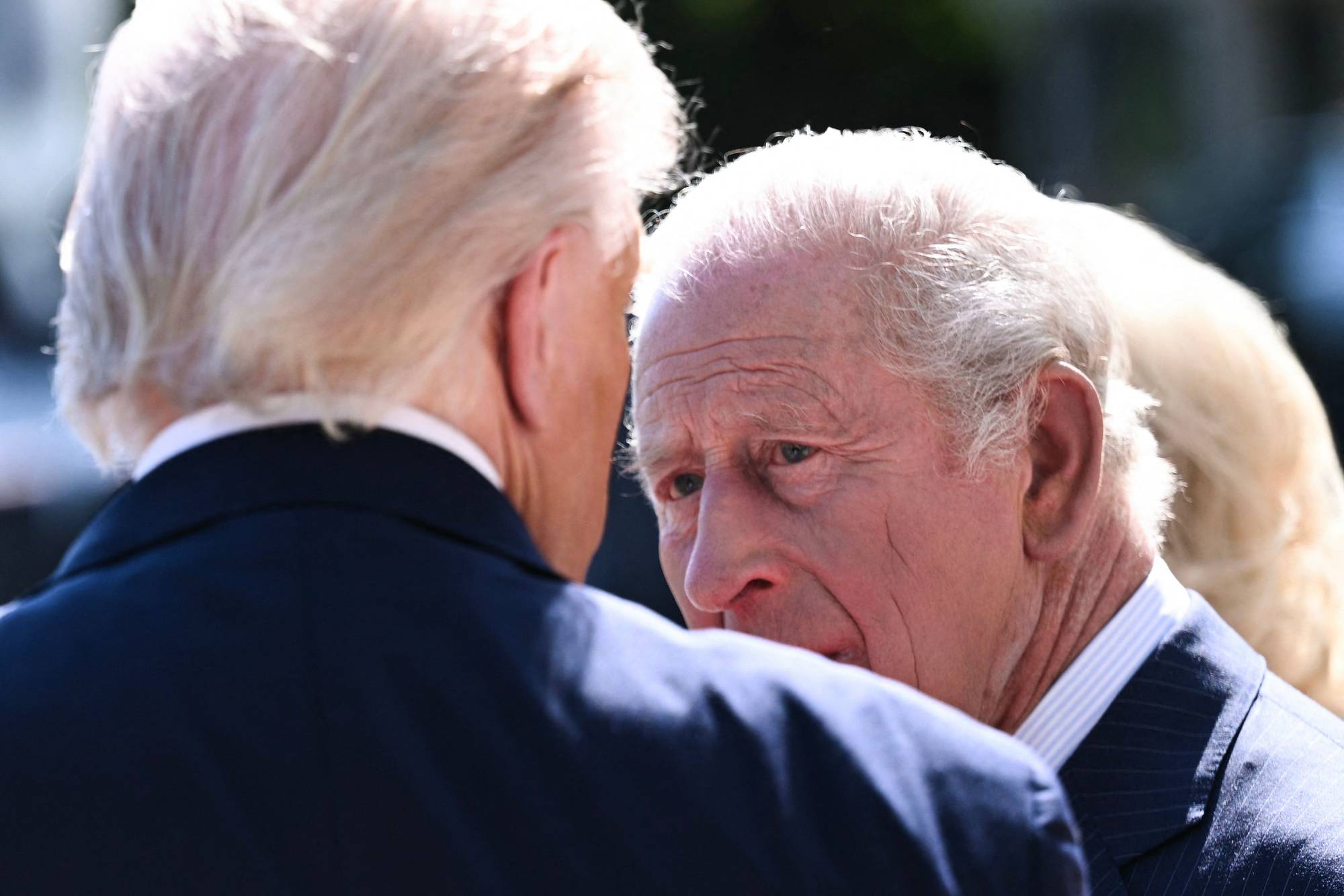 Kong Charles III snakker med Donald Trump. Begge mennene er kledd i mørke dresser. Bildet er tatt utendørs i dagslys. (Bildebeskrivelsen er laget av en KI-tjeneste)