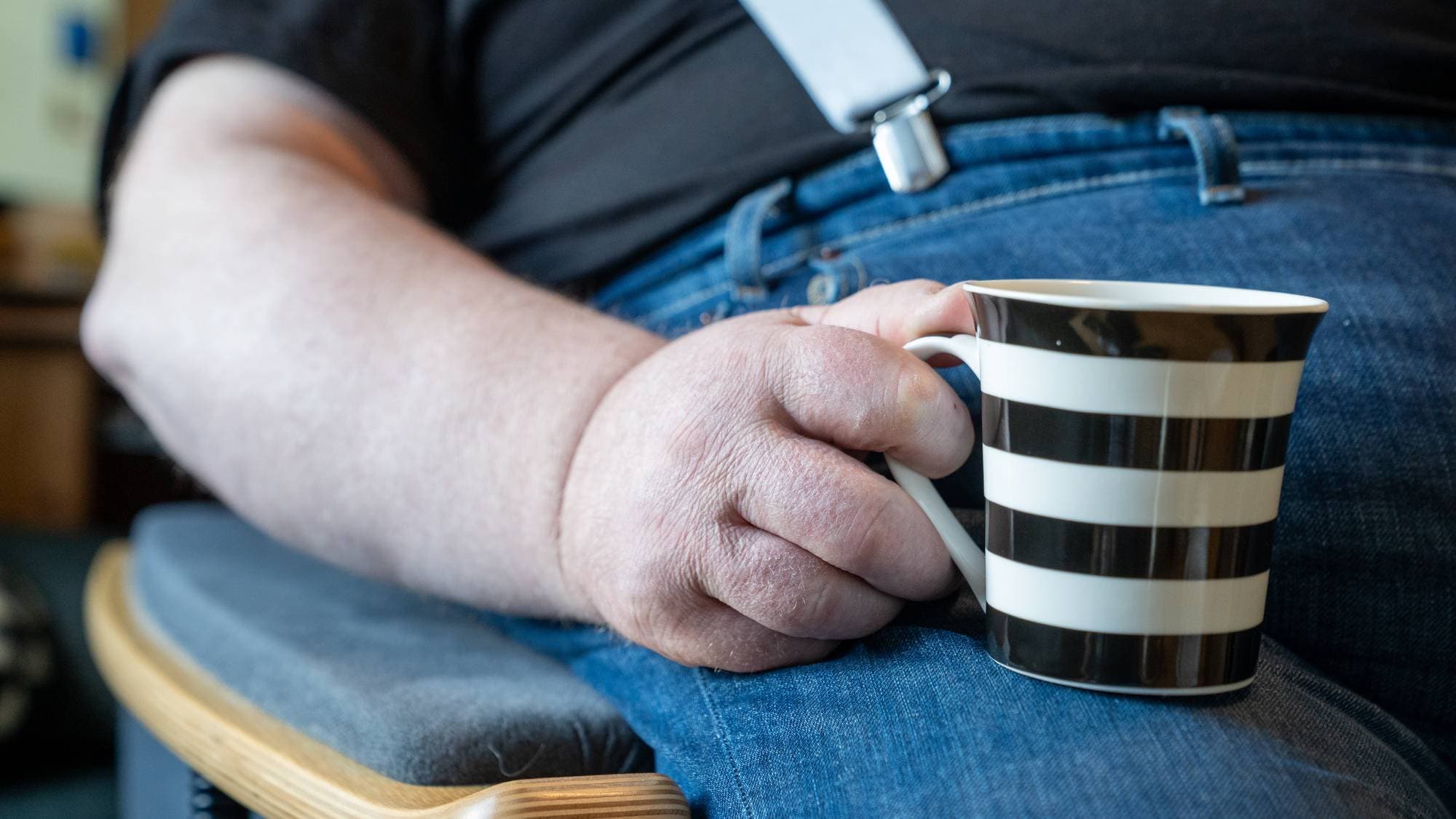 Mann holder stripete kaffekopp i handa.