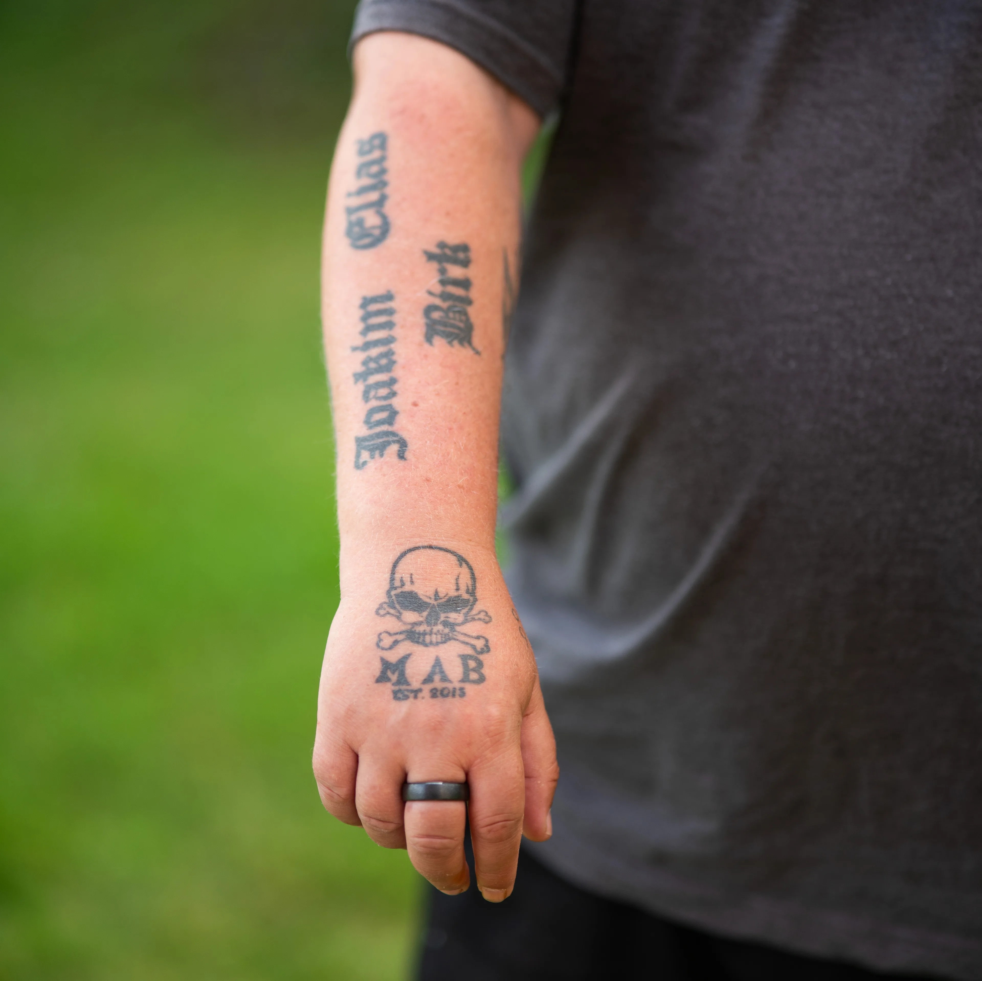 Arm med tatoveringer av navn og et hodeskallemotiv, samt en ring på fingeren. (Bildebeskrivelsen er laget av en KI-tjeneste)