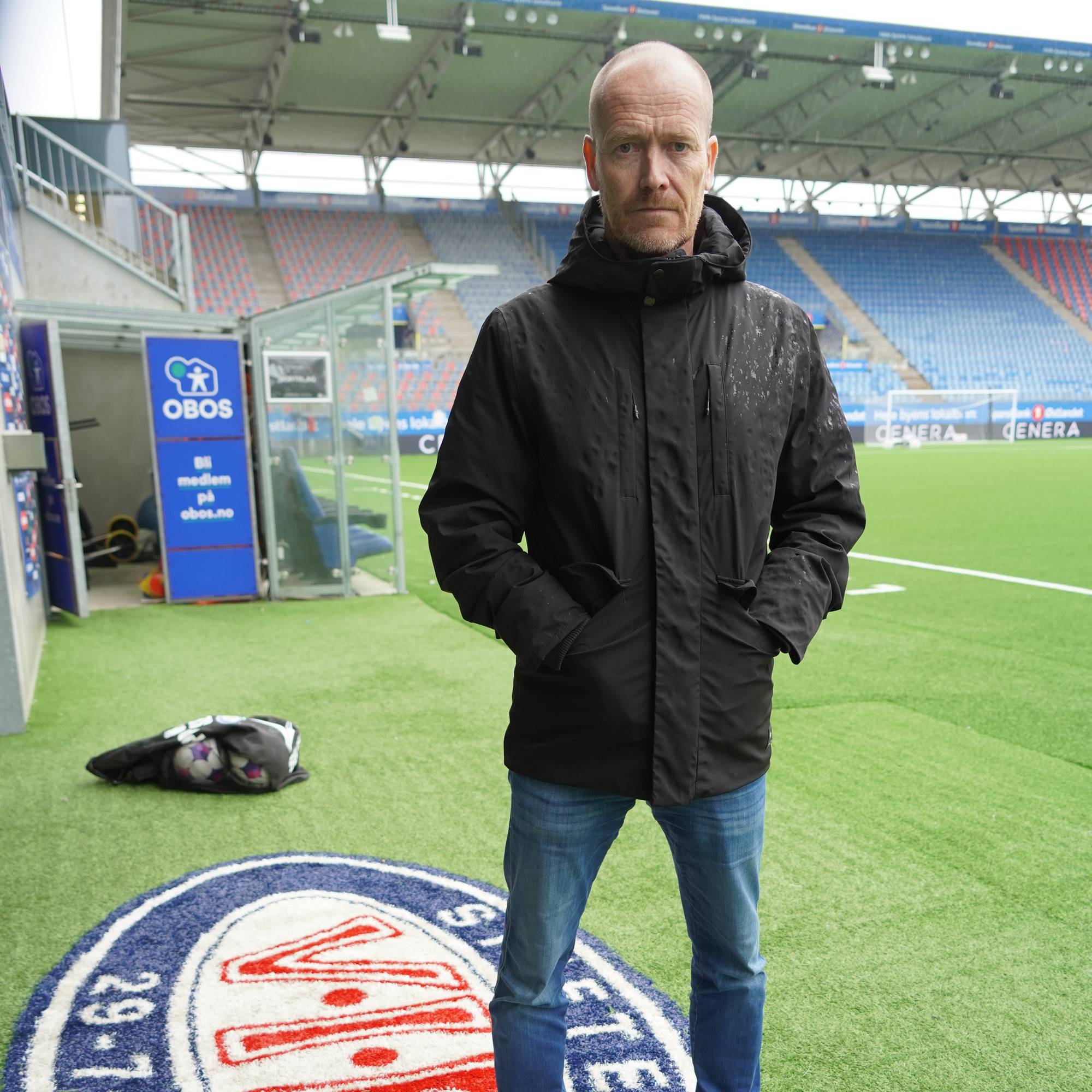 Mann i svart jakke avbildet på fotballstadion