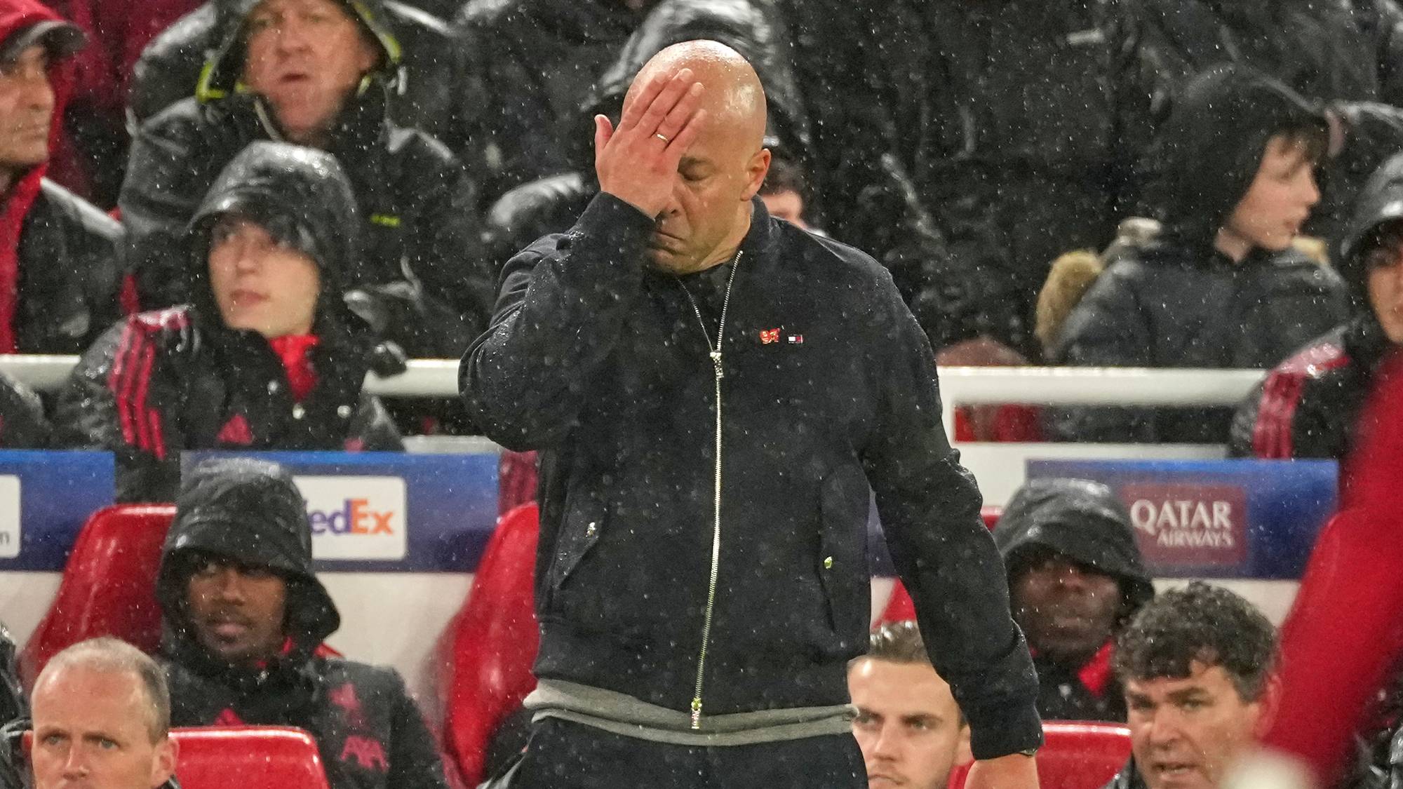 En mann holder hånden mot pannen mens han står under regn. Han er omgitt av andre personer på en tribune. En skjerm med NTB-logo er plassert foran mannen. (Bildebeskrivelsen er laget av en KI-tjeneste)