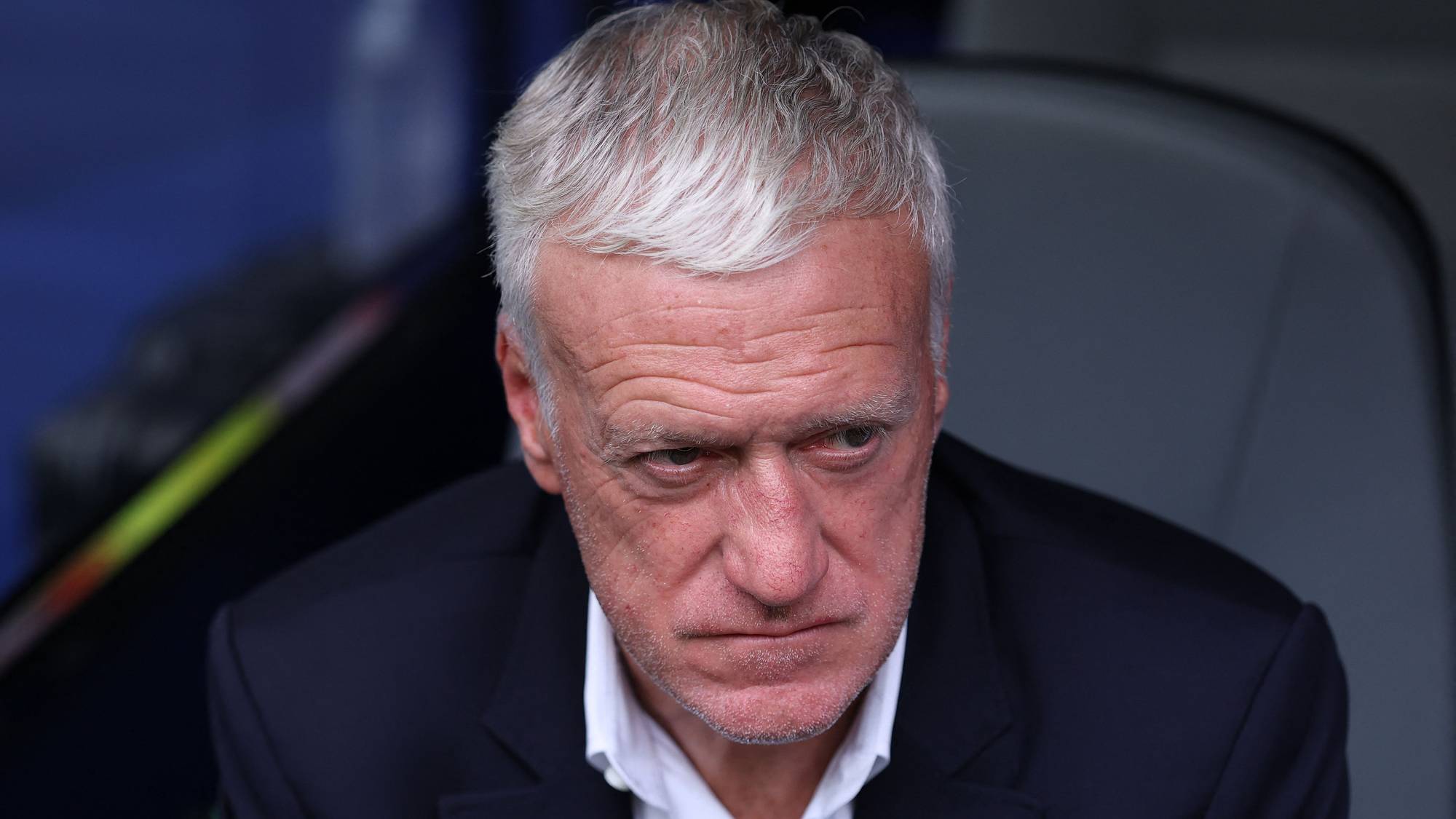 Didier Deschamps sitter i en mørk dressjakke og hvit skjorte. Han ser ned med et alvorlig blikk. (Bildebeskrivelsen er laget av en KI-tjeneste)
