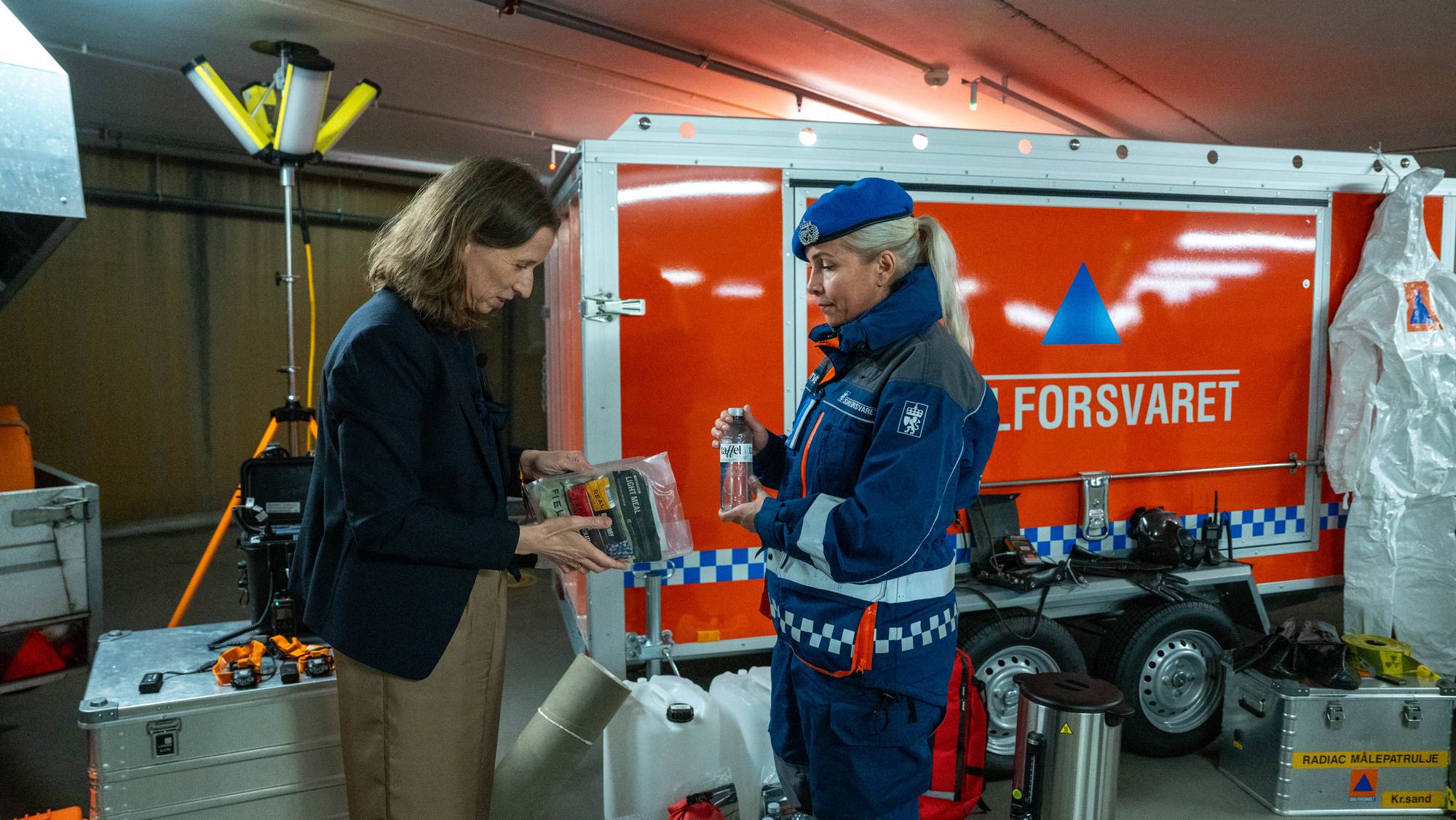 To kvinner og en kvinne står i et rom med en oransje bil (Bildebeskrivelsen er laget av en KI-tjeneste)