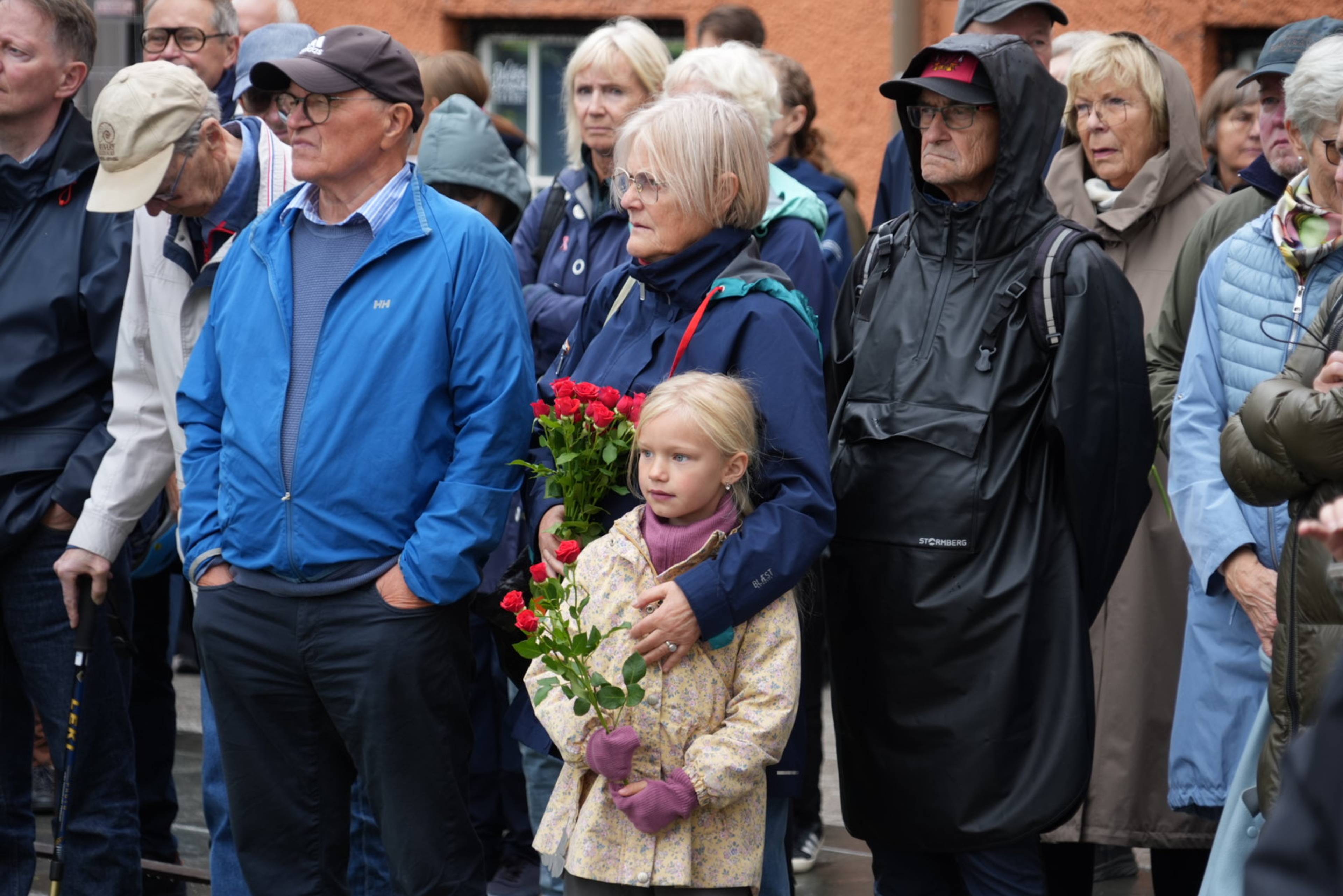 En gruppe mennesker står samlet utendørs, der en kvinne holder rundt en jente med røde roser.
