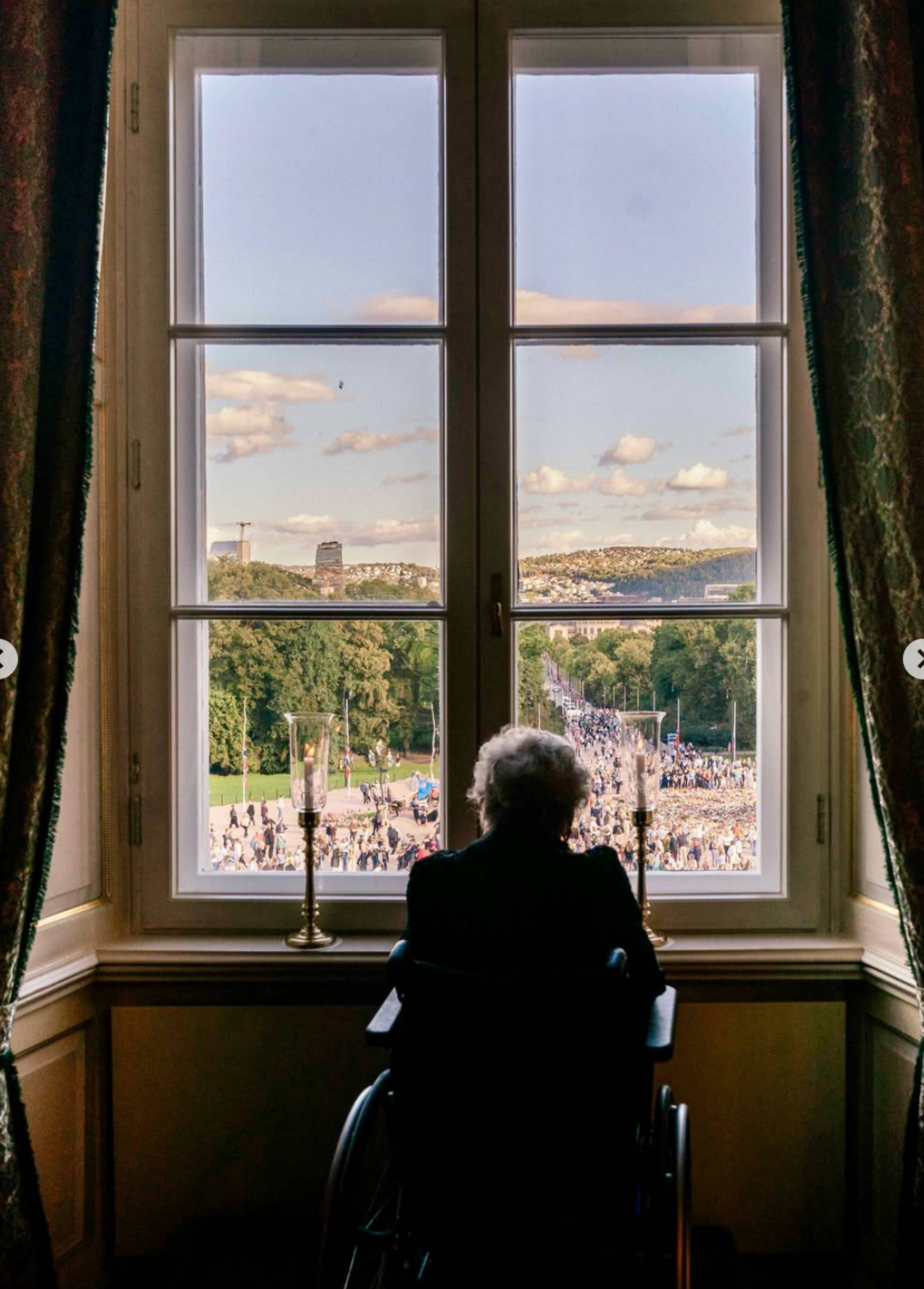 Prinsesse Astrid kikker ut av vinduet på Slottet. Hun ser ut på folkemengden.