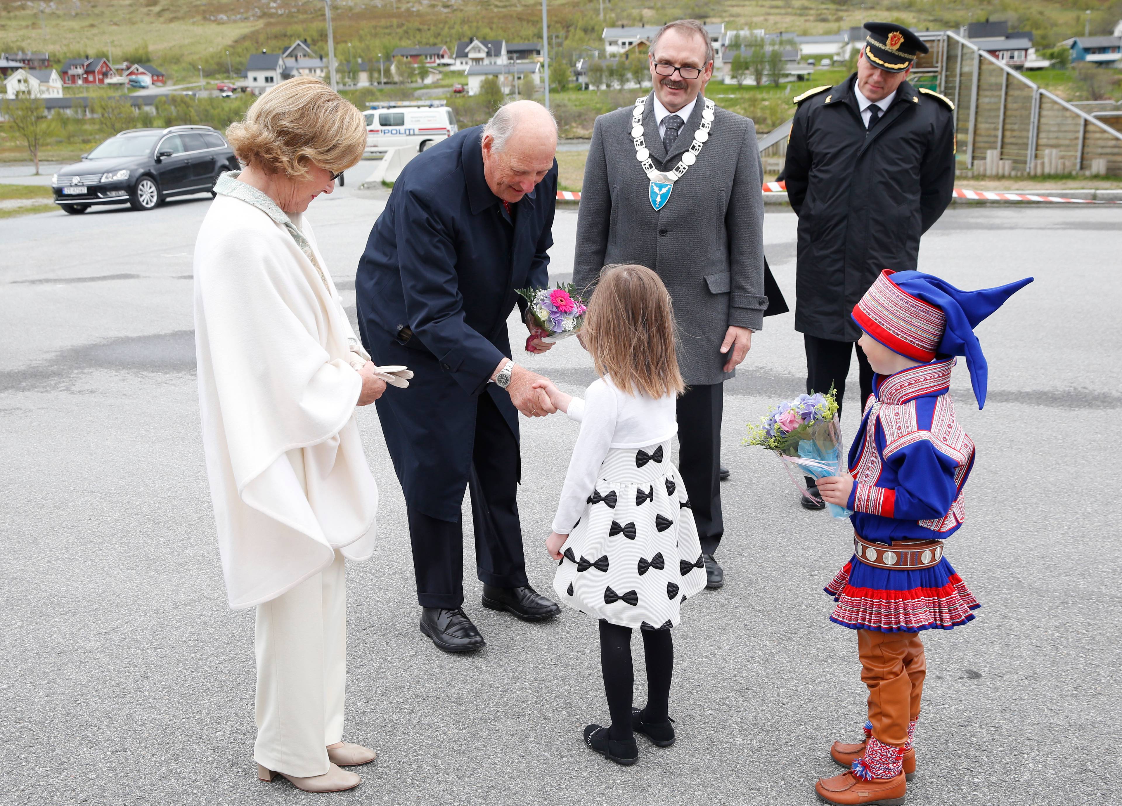 Kong Harald og dronning Sonja hilser på to barn som overrekker kongeparet blomster.