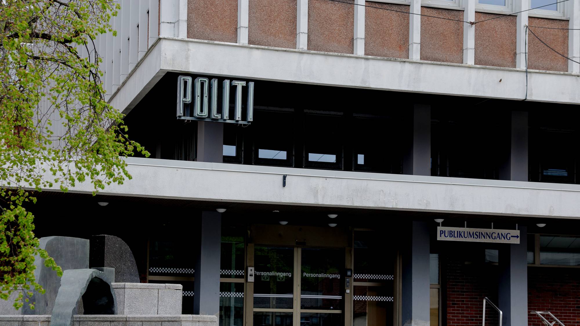 Inngangen til en politistasjon med en skulptur på trappen foran. (Bildebeskrivelsen er laget av en KI-tjeneste)
