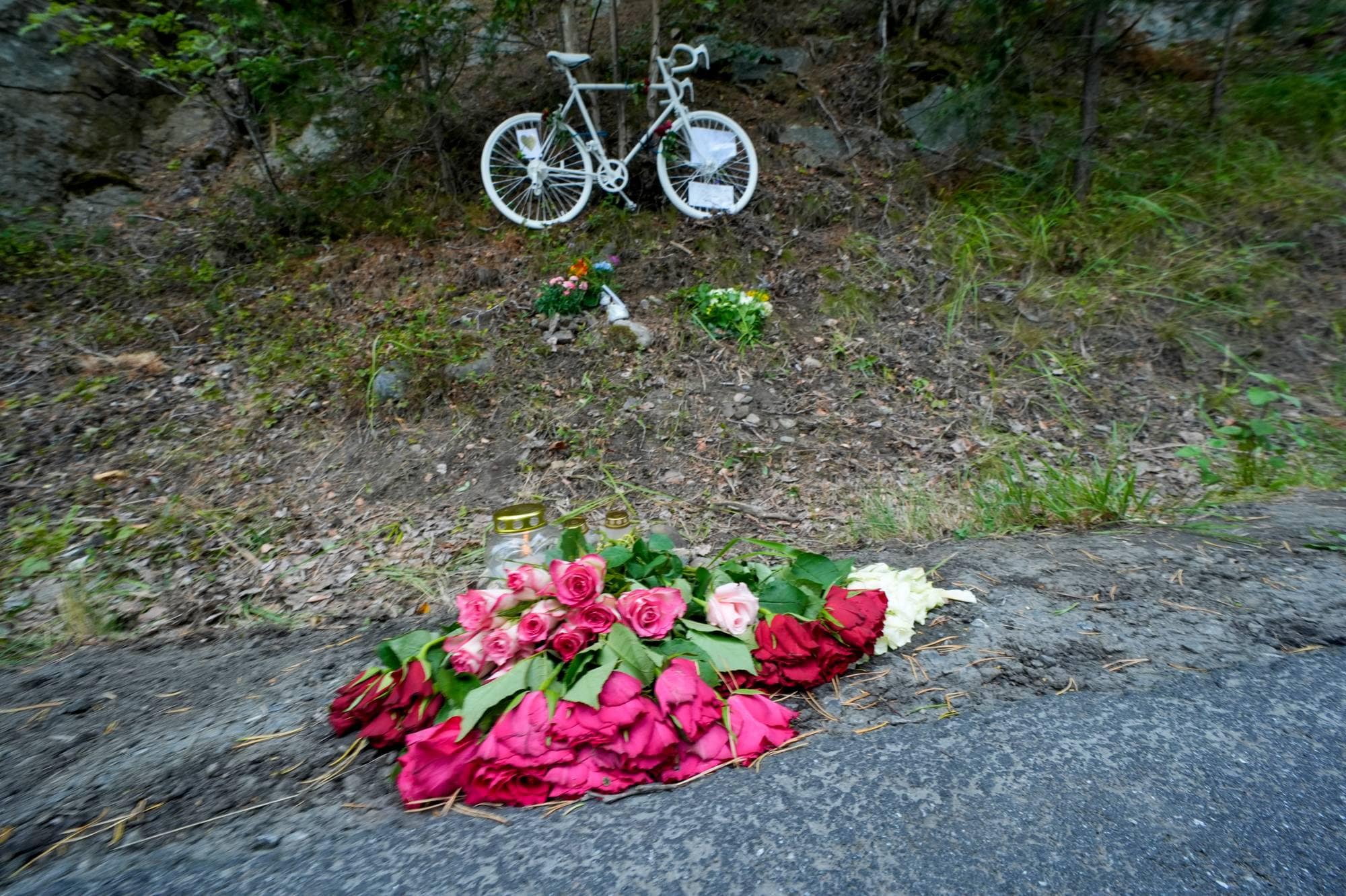 En hvit sykkel og blomster er plassert ved en vei som et minnesmerke. (Bildebeskrivelsen er laget av en KI-tjeneste)