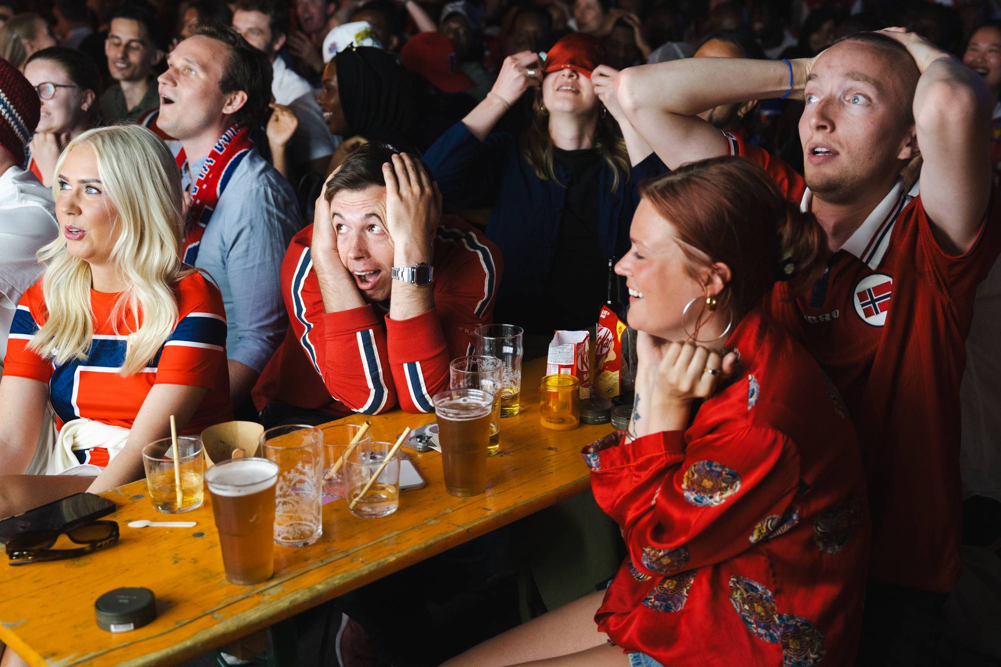 Publikum sitter ved bord med drikke og reagerer med sterke ansiktsuttrykk mens de ser på en kamp. Hanna Begby, Jon Bugge Maruissen, Helena Riise Undall, Dam Gjermund Moon-at, Simone Storm, Iselin Sørum, Johannes Riise Undall og Edvard Undall ser kampen på Oslo Street Food.