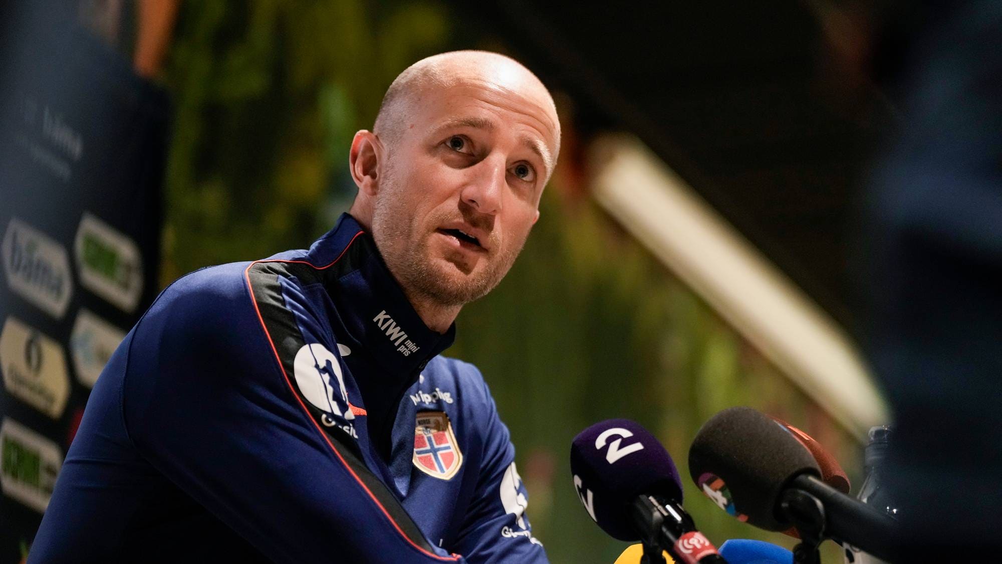 Brede Hangeland snakker i mikrofoner under en pressekonferanse. Han er kledd i landslagsdrakt. (Bildebeskrivelsen er laget av en KI-tjeneste)