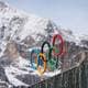 Claudia Greco / Reuters / NTB De olympiske ringene er plassert på en plattform foran snødekte fjell. Ringenes farger inkluderer blå, svart, rød, gul og grønn. Det er halvmørke skyer i bakgrunnen, som gir et dramatisk preg. Omgivelsene indikerer en kald værtype, typisk for vinteren. (Bildebeskrivelsen er laget av en KI-tjeneste)