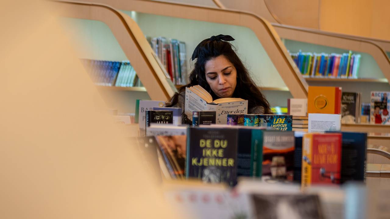 Cristina Berki leser i en bok på biblioteket i Vennesla