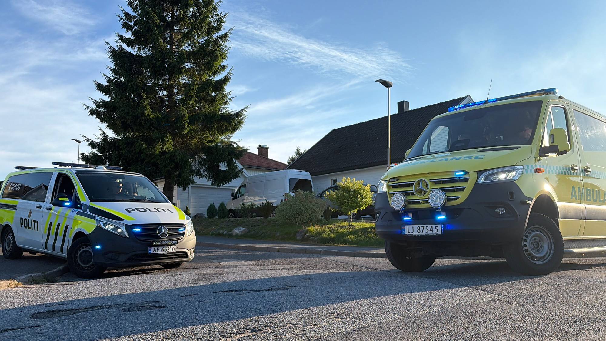 Politi- og ambulansebil står parkert i et boligområde med blålys tent. (Bildebeskrivelsen er laget av en KI-tjeneste)