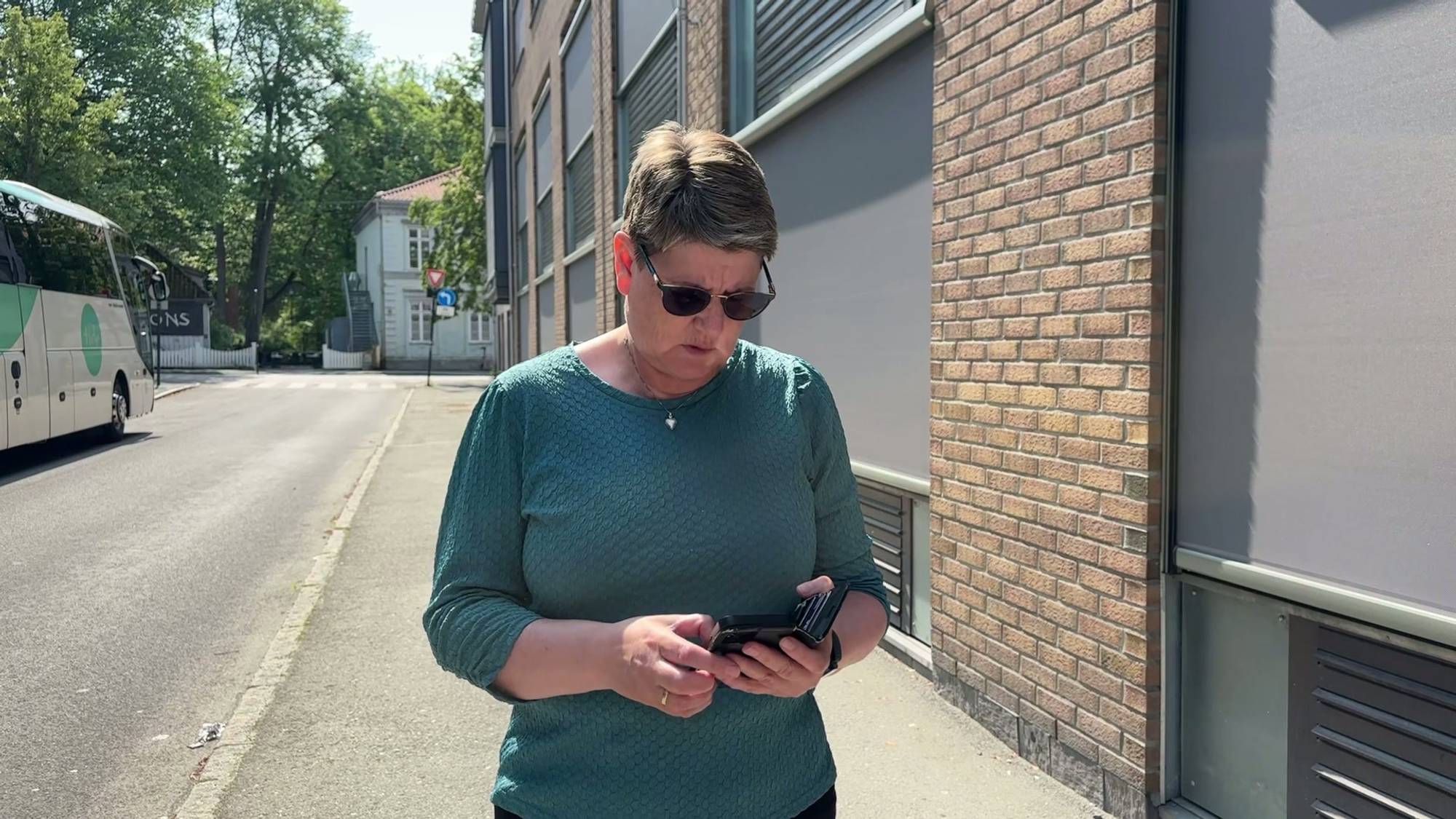 En kvinne med kort hår og grønn genser ser på telefonen sin