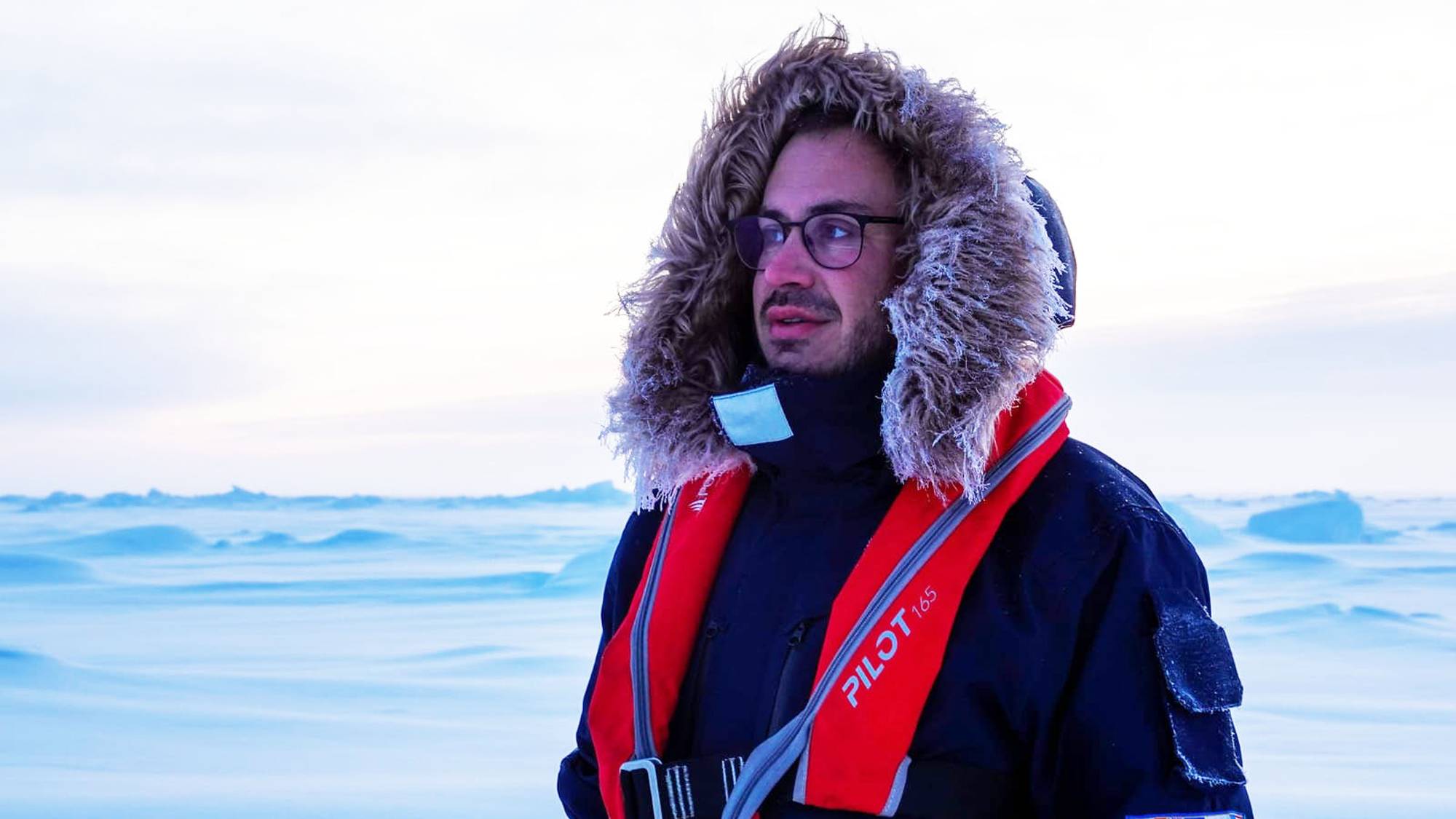 En mann i parkas og rød redningsvest på i et polart landskap. 