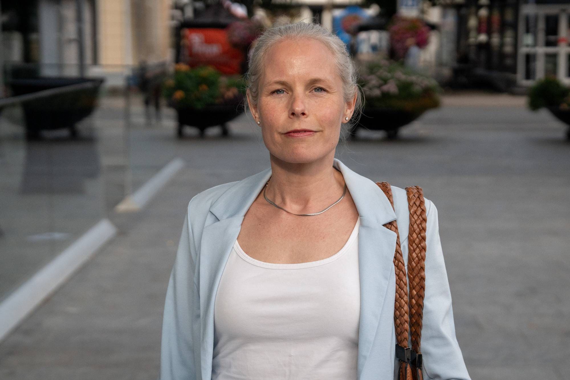 Kvinne med lyseblå blazer og hvit topp med tilbaketrukket hår ser rett i kamera.