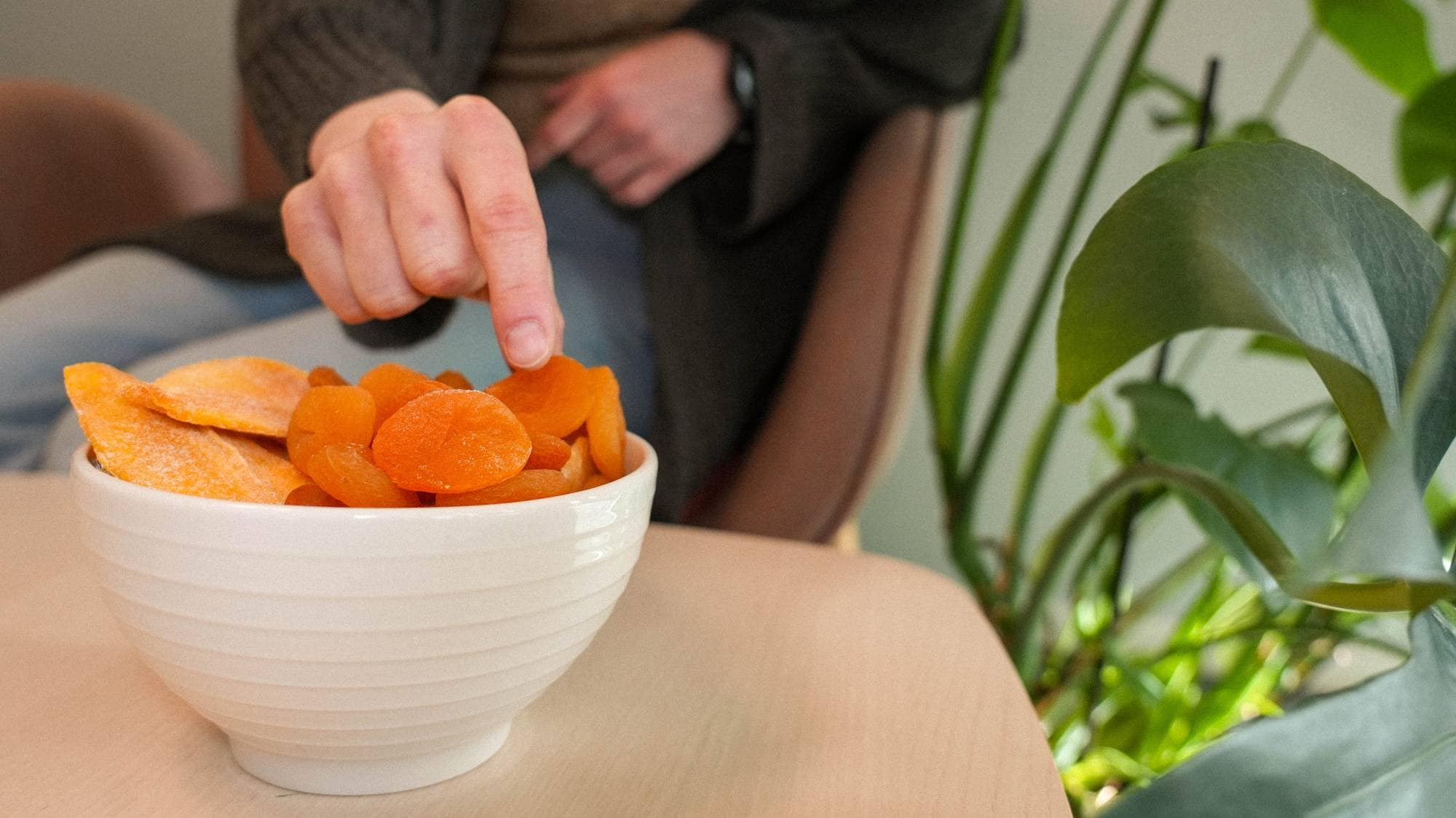 Tørket frukt. Hånd plukker aprikos fra skålen.