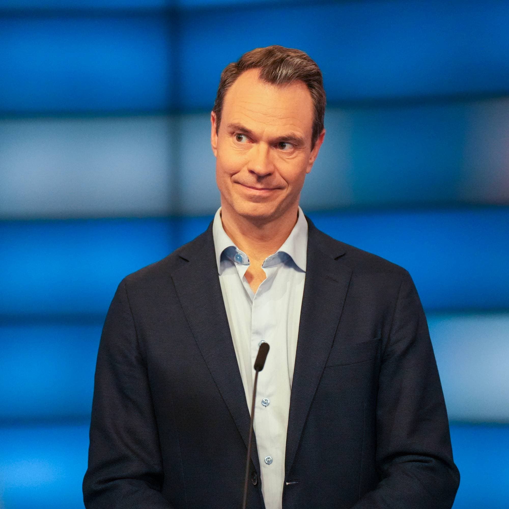 En mann i dress står framfor en talerstol med mikrofon framfor se. 