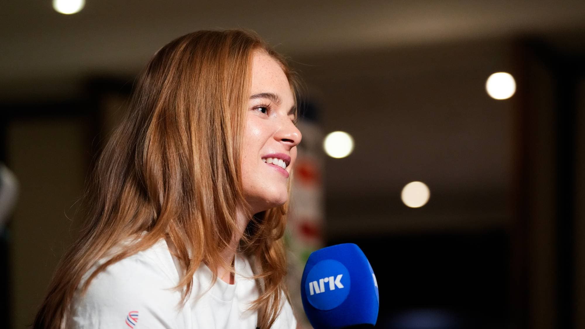En ung kvinne med langt brunt hår intervjues av NRK. (Bildebeskrivelsen er laget av en KI-tjeneste)