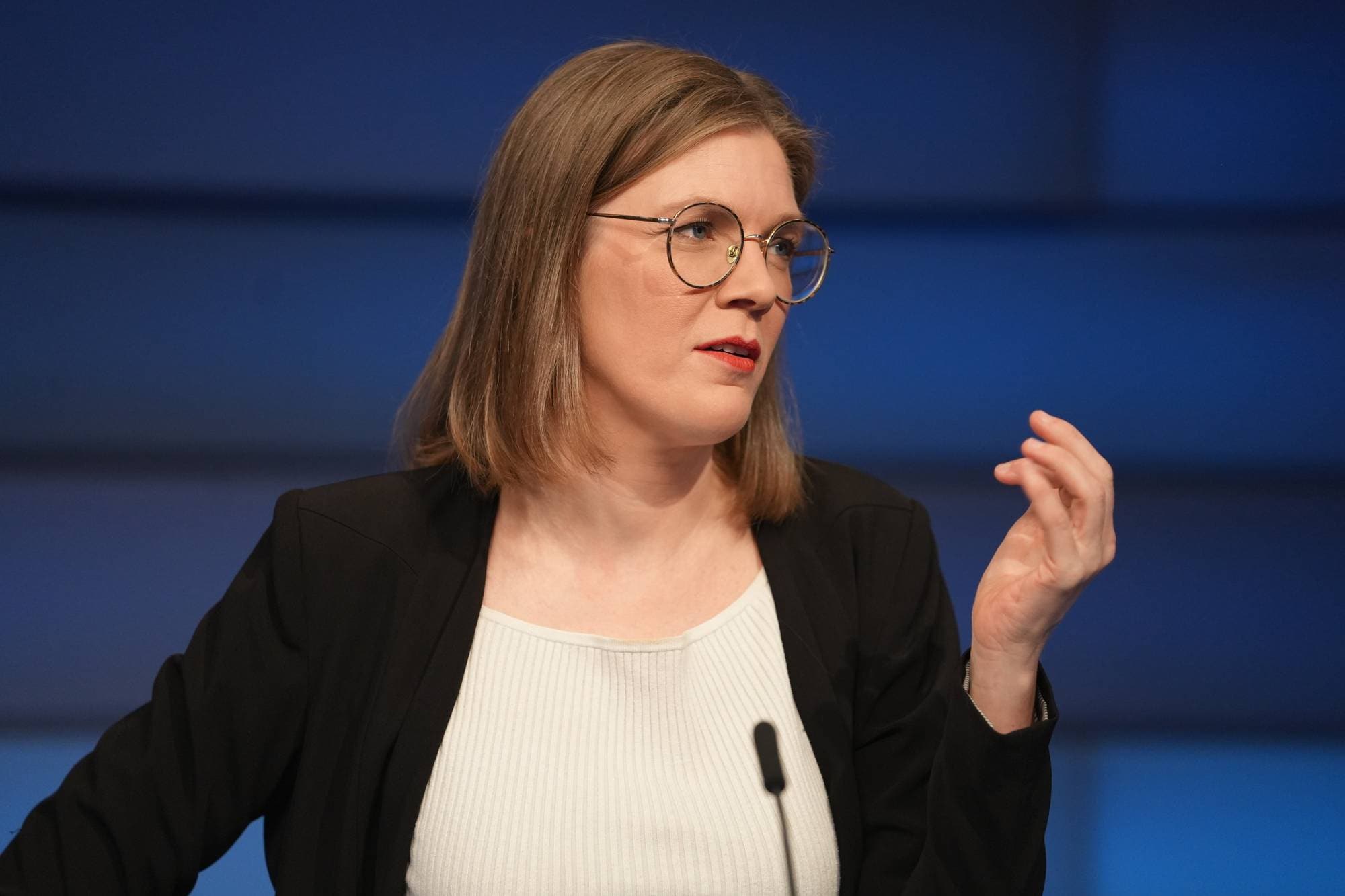 Marie Sneve martiniussen med briller snakker foran en blå bakgrunn. (Bildebeskrivelsen er laget av en KI-tjeneste)