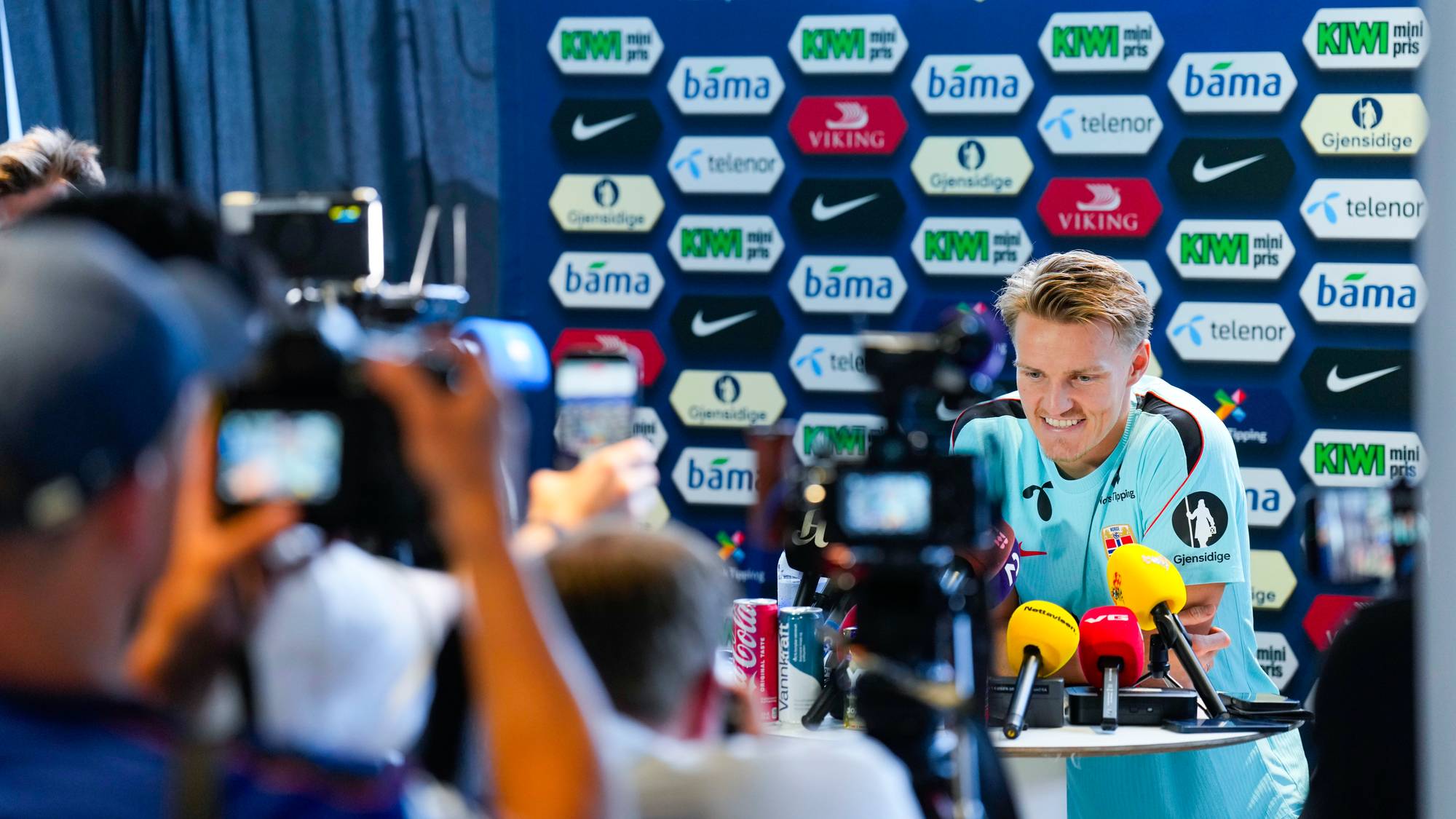 Martin Ødegaard sitter foran pressefolk på en pressekonferanse med sponsorvegger i bakgrunnen. (Bildebeskrivelsen er laget av en KI-tjeneste)