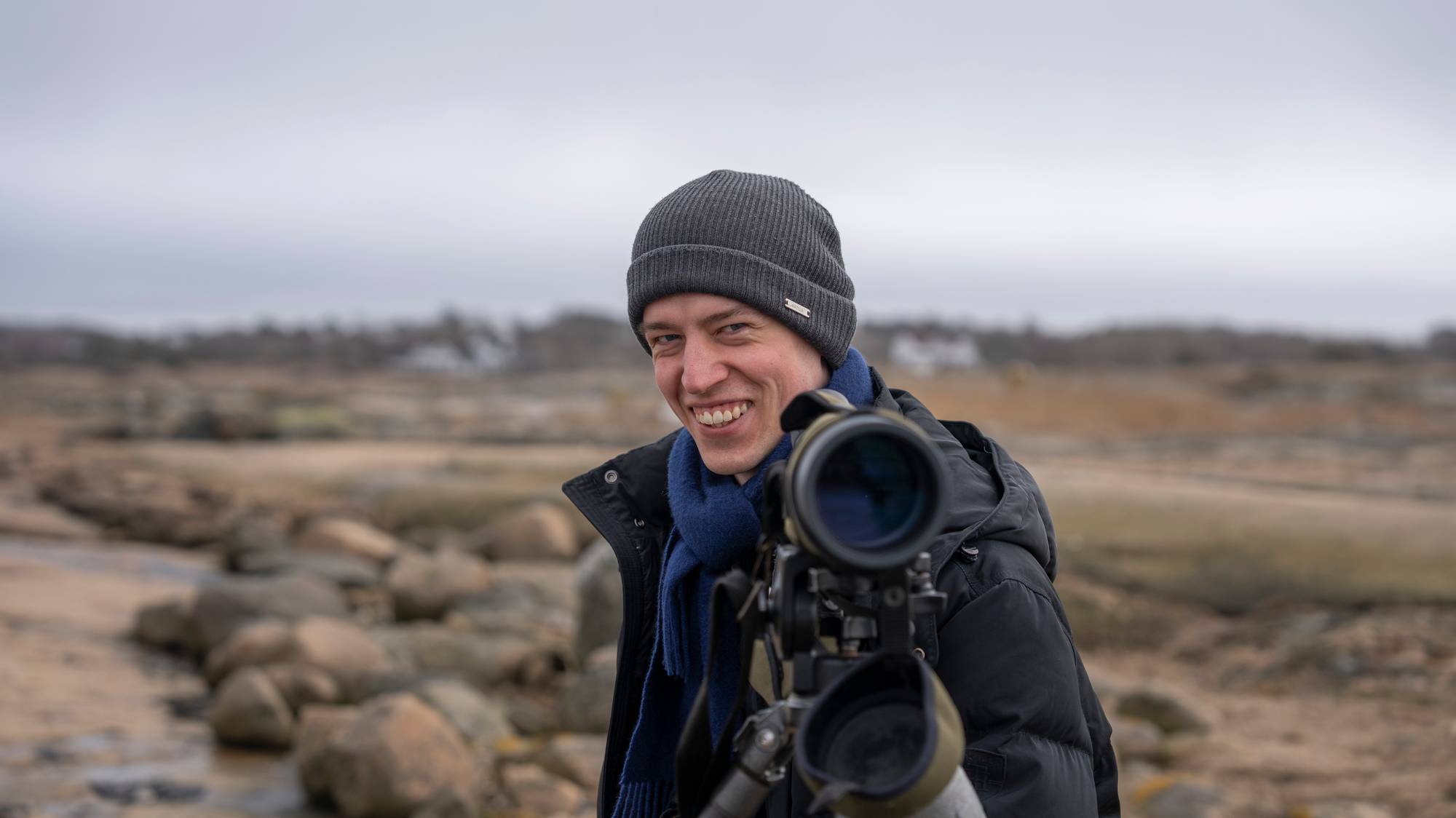 En mann står med en kikkert i er flatt skjærgårdslandskap