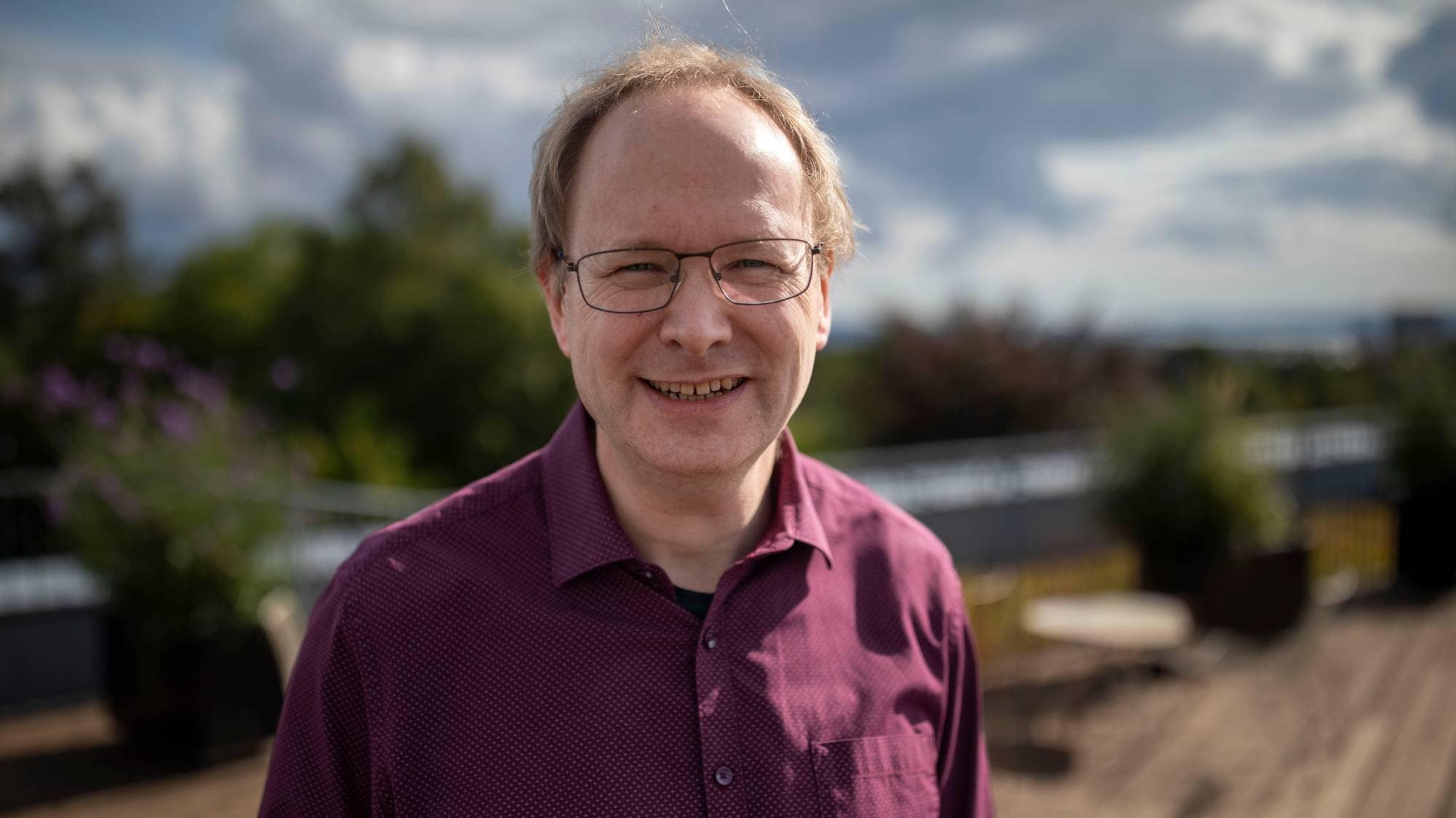 Nils Fearnley, forsker ved Transportøkonomisk Institutt (TØI). Nils har kort, lyst hår, briller med svart innfatning og har på seg en plommefarget skjorte. Han smiler svakt mot kameraet.