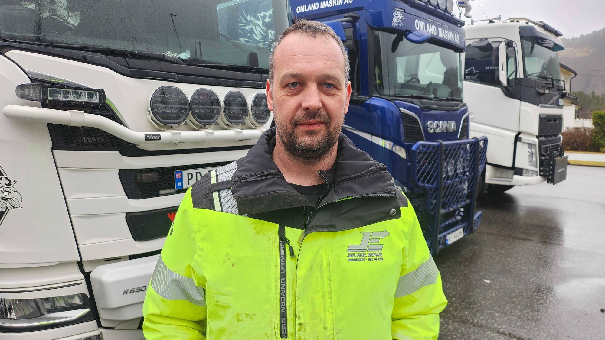 viser en mann i gul jakke foran flere lastebiler