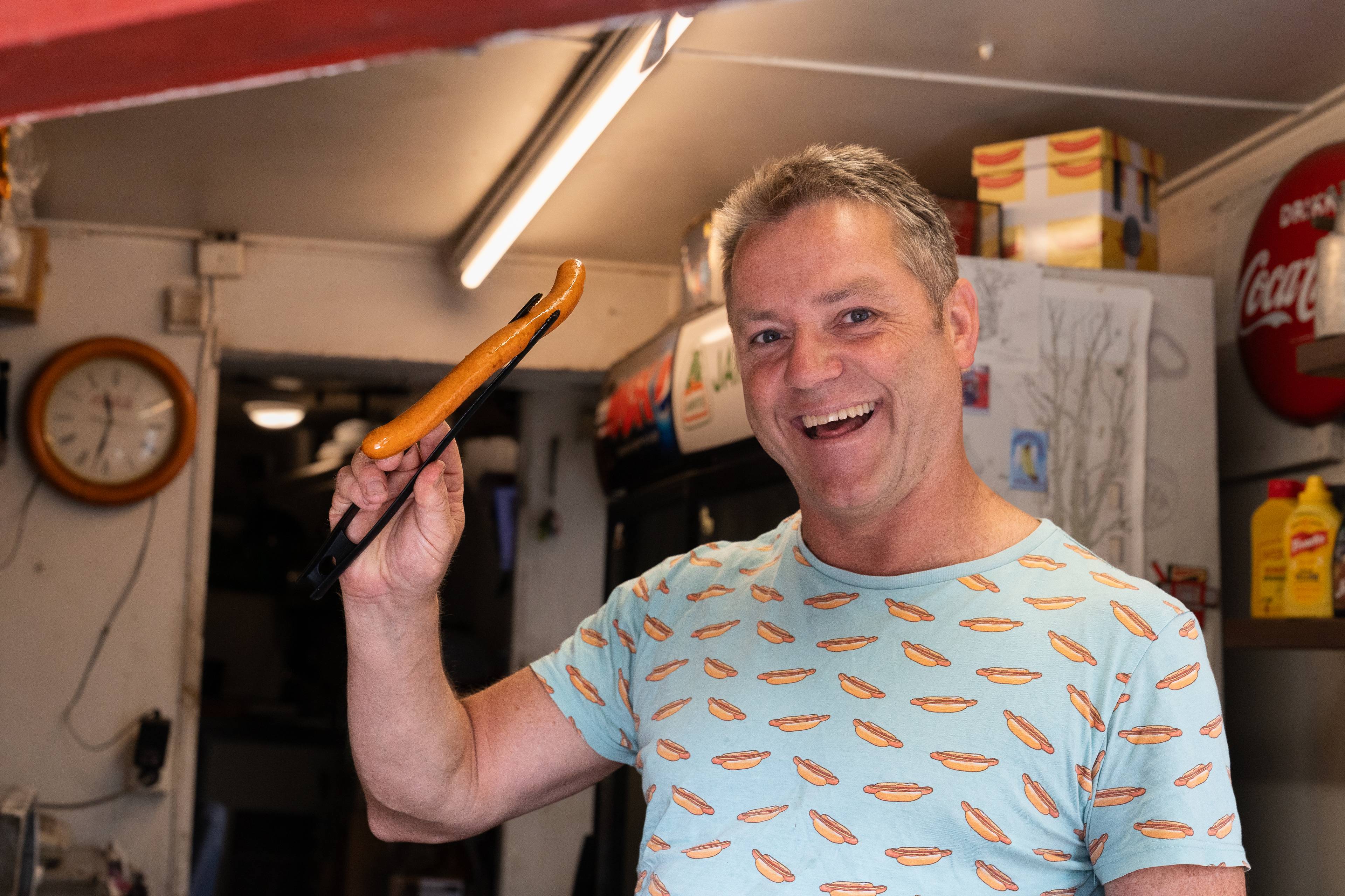 en mann holder en pølse med en klype og smiler