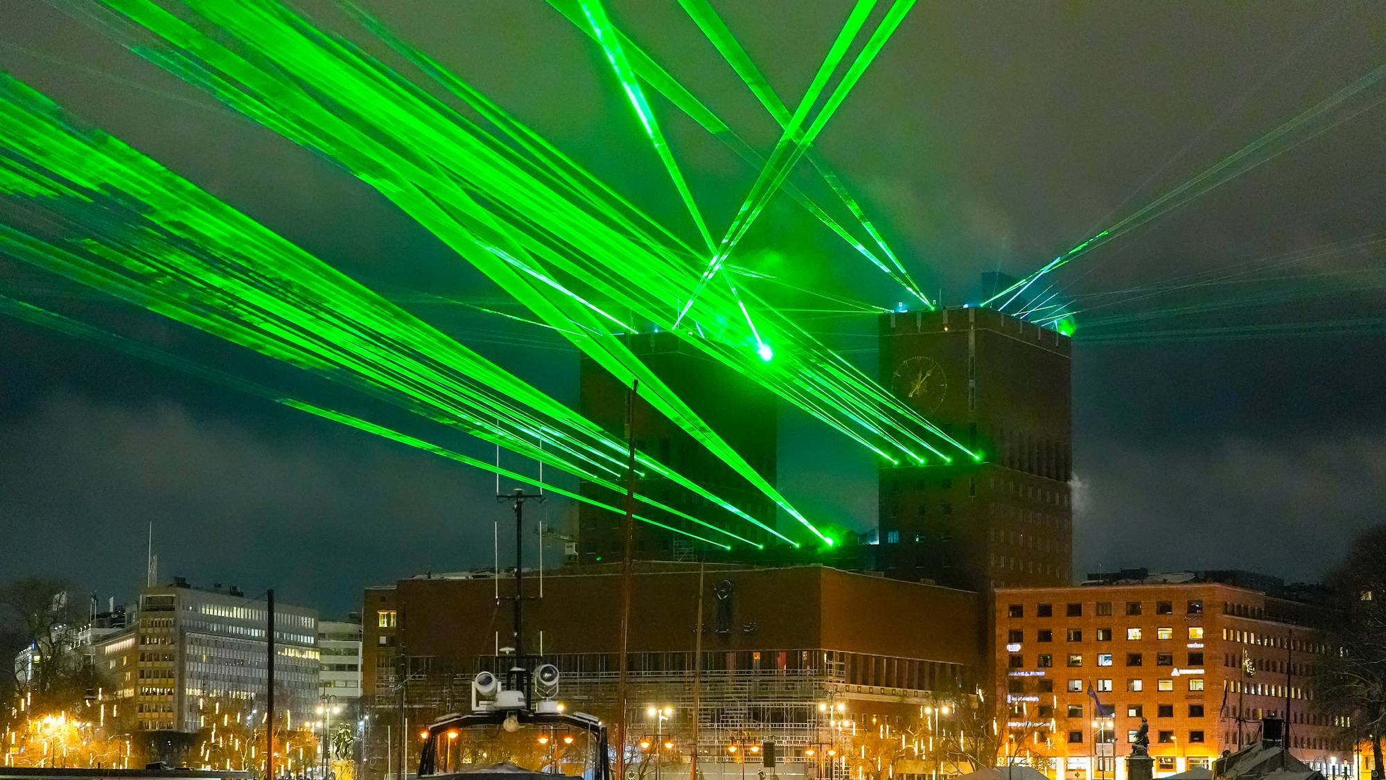 Grønne laserstråler lyser opp nattehimmelen over Oslo rådhus. (Bildebeskrivelsen er laget av en KI-tjeneste)