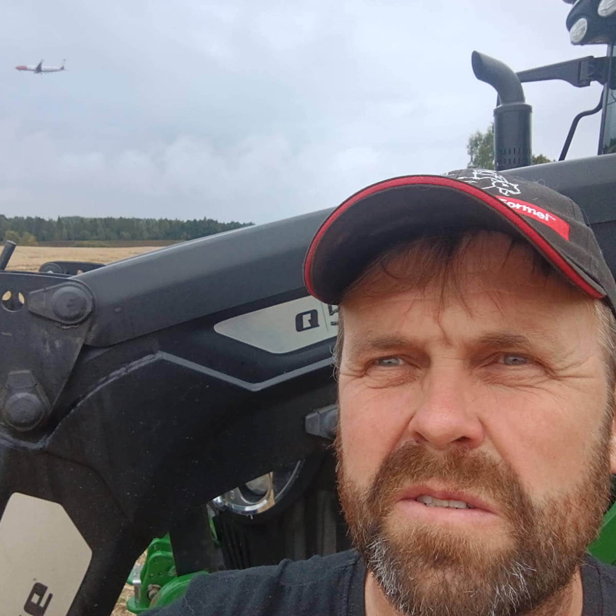 Bildet viser en mann med caps. I bakgrunnen ser man et fly på himmelen