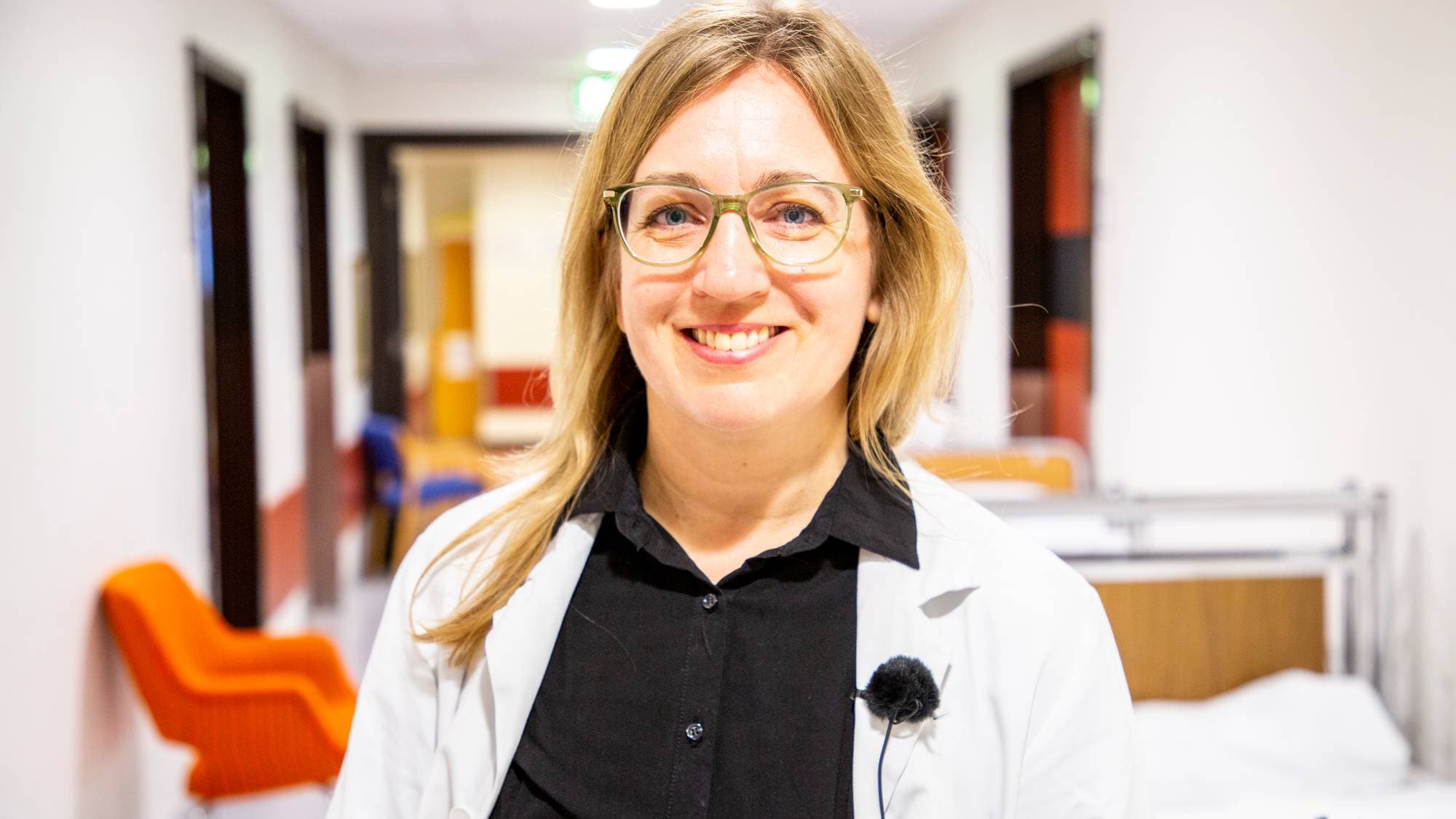 Karoline Lode-Kolz står i ein gang på Stavanger universitetssjukehus. Ho smiler. Bak ho ser ein senger og stolar, samt dører til andre kontor på SUS.