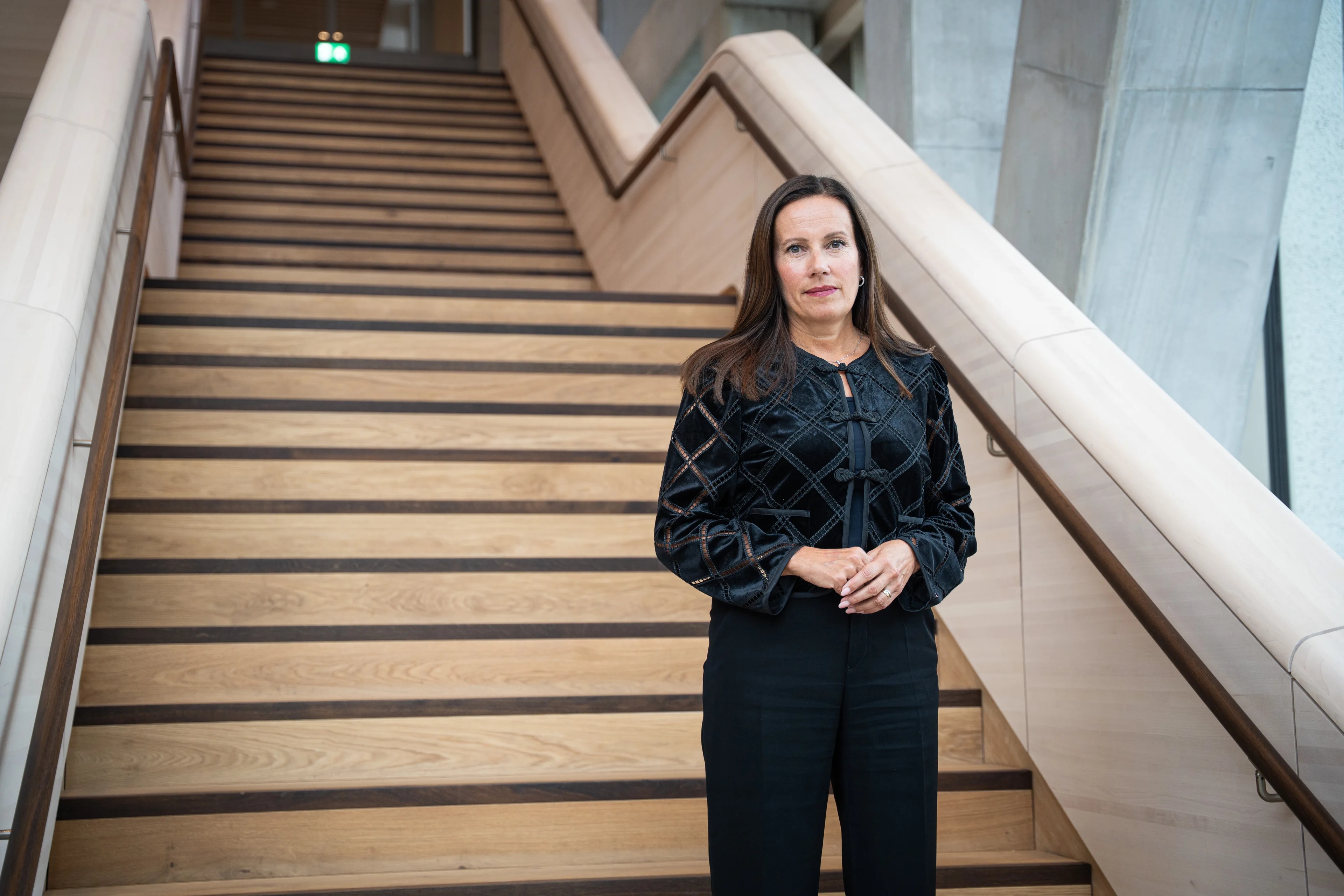 Kvinne med svart topp og mørkt hår står i en trapp i Regjeringskvartalet. Trappen er ny og i tre.