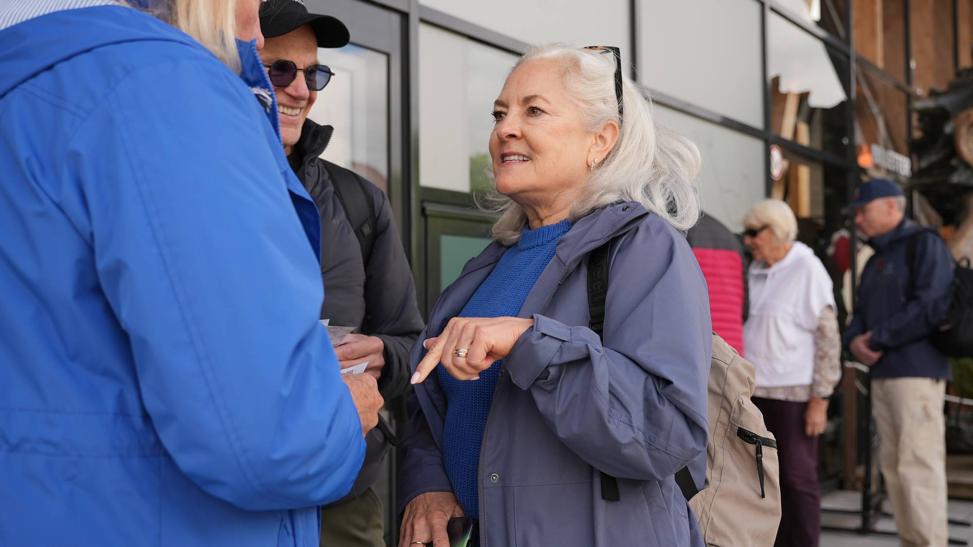 En gruppe mennesker snakker sammen utenfor. En kvinne i blå jakke snakker med en mann med solbriller og caps. I bakgrunnen står to andre personer. (Bildebeskrivelsen er laget av en KI-tjeneste)