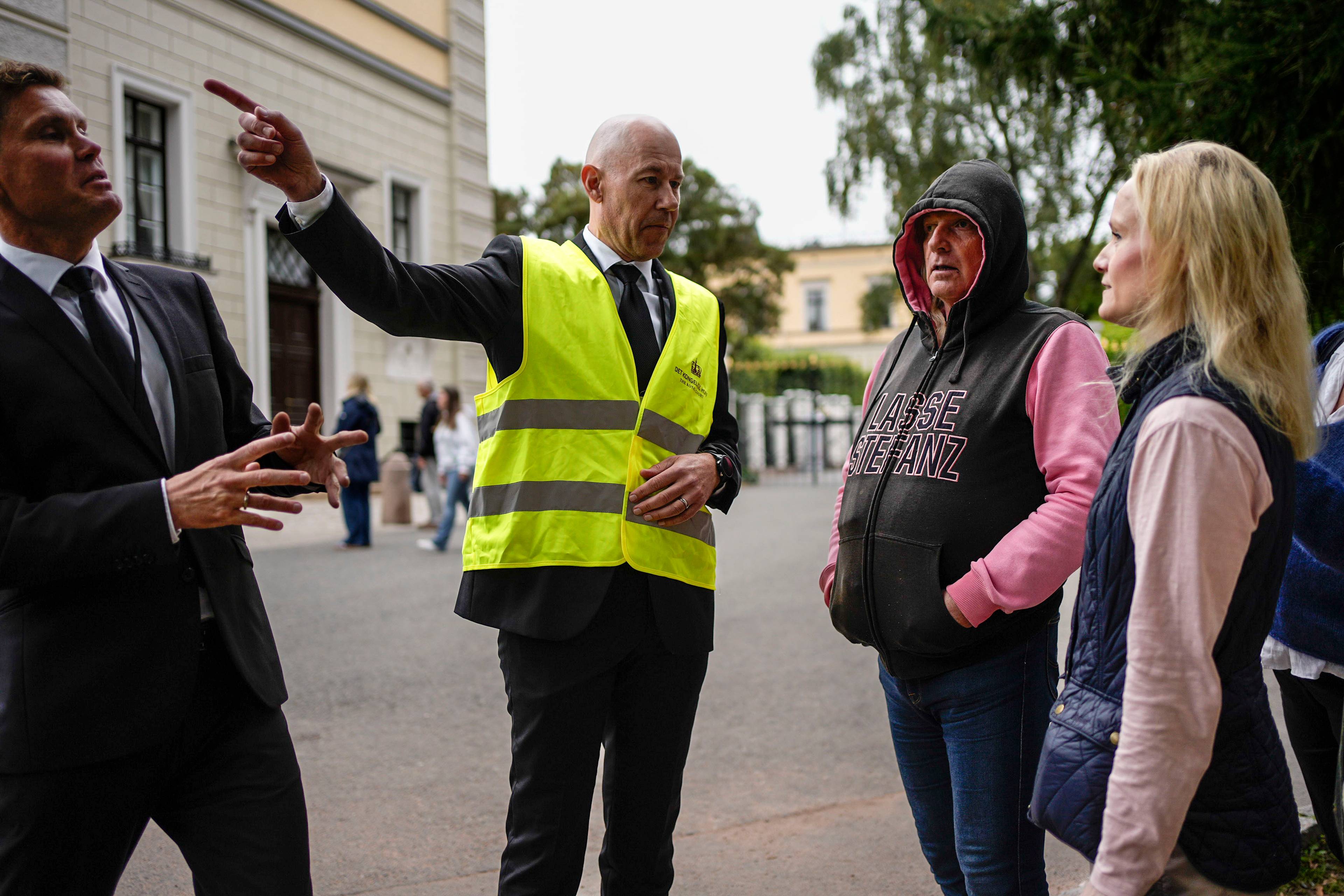 en vakt i gul vest som snakker med en gruppe mennesker (Bildebeskrivelsen er laget av en KI-tjeneste)