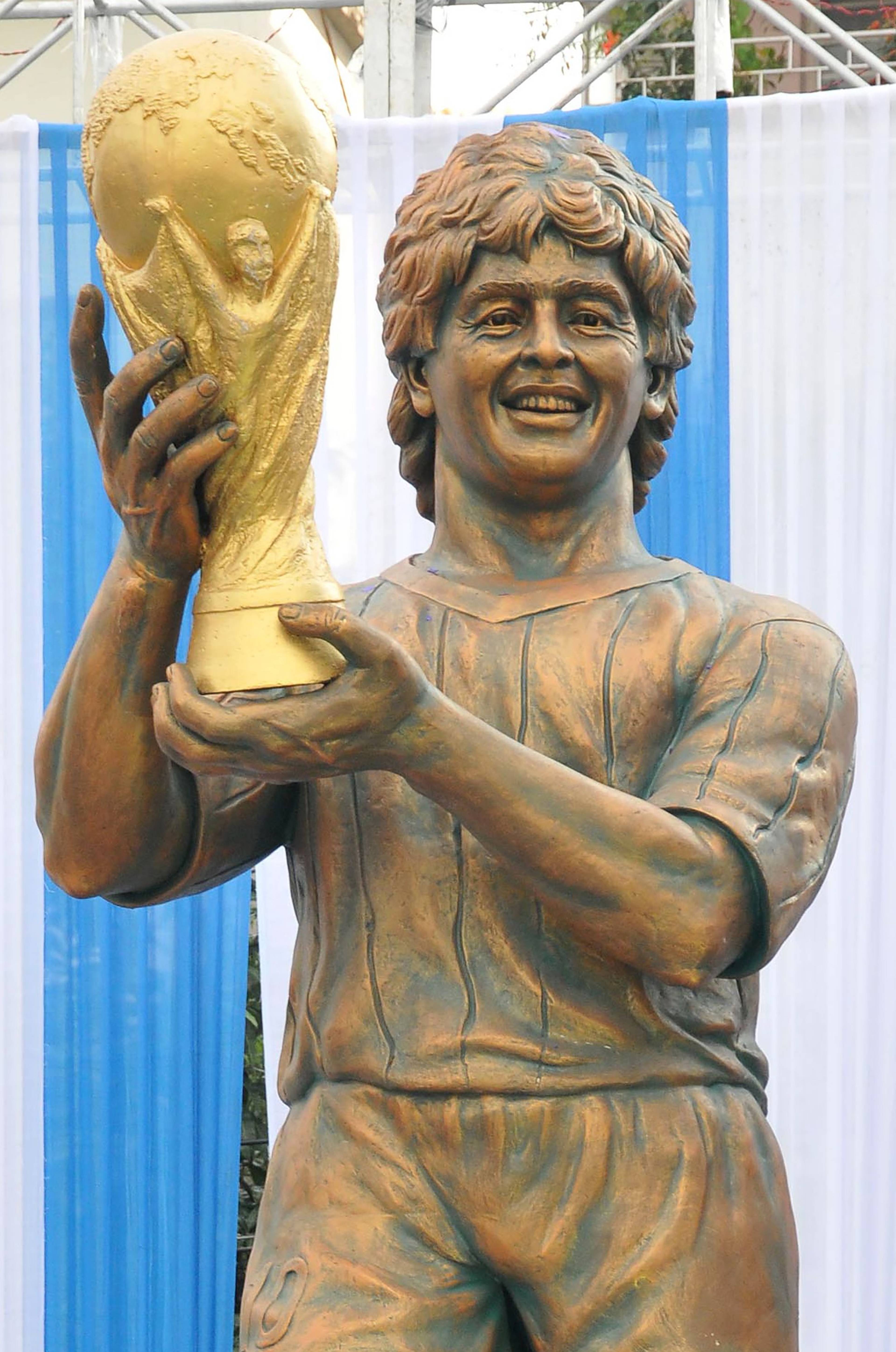 Bronsestatue av Diego Maradona som holder VM-trofeet, plassert framfor blå og kvite tekstilar. (Bildebeskrivelsen er laget av ein KI-teneste)