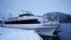 Øyvind Sandnes/NRK En hvit båt er fortøyet ved en kaifront, omkranset av snødekte fjell og en grålig himmel. To personer står på dekk og ser mot land. Det er snø på både kaien og båten. Omgivelsene gir inntrykk av vinterforhold.