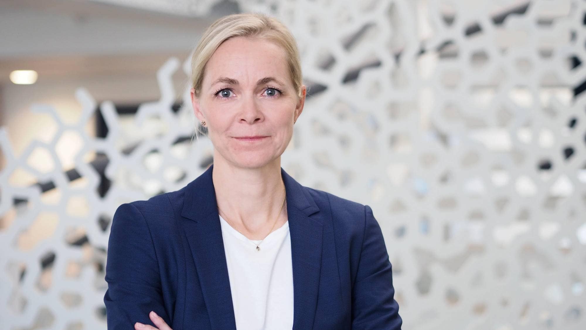 Kvinne med blondt hår og mørkeblå blazer ser i kamera