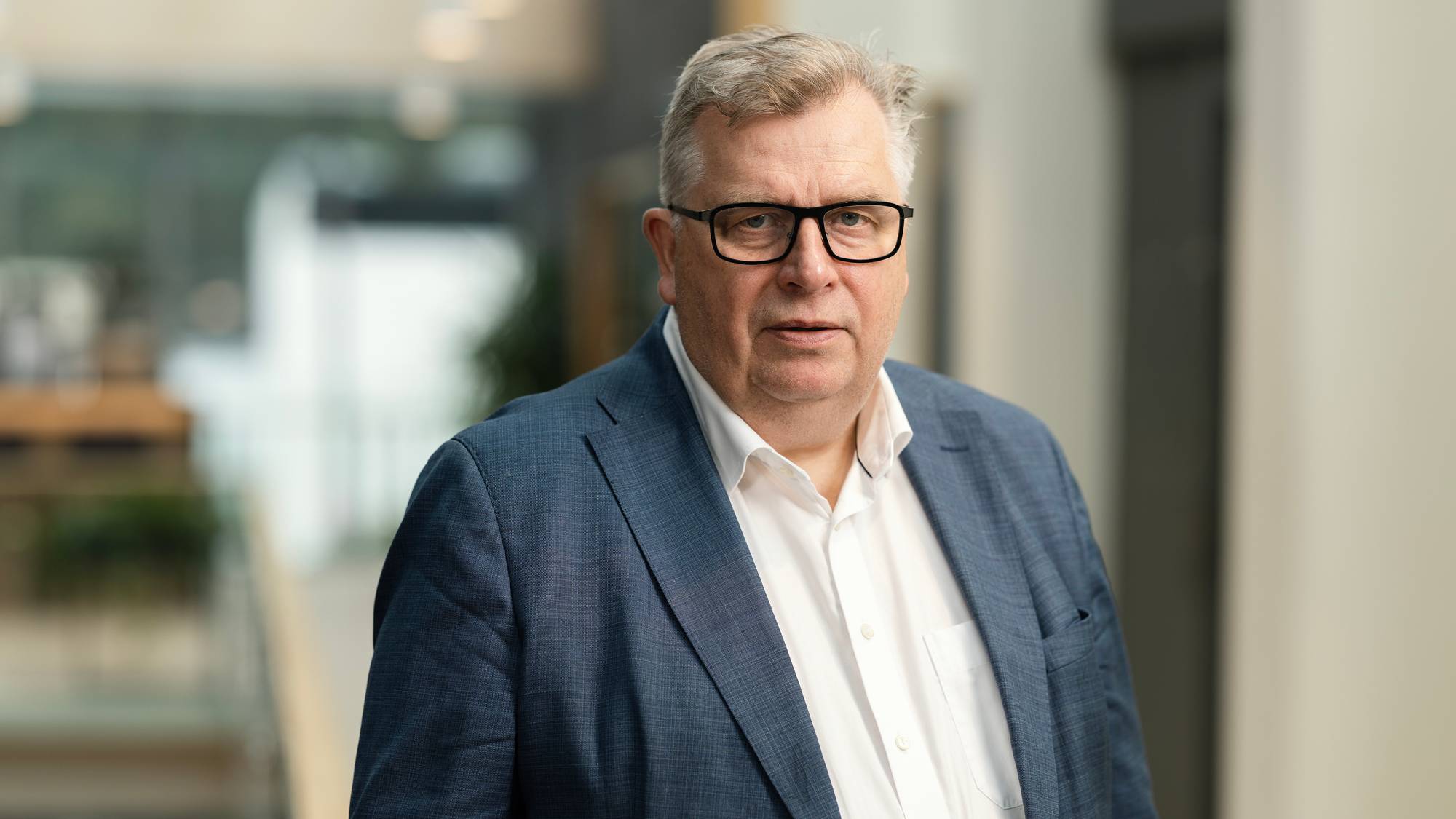 Mann i hvit skjorte, briller og dressjakke ser i kamera