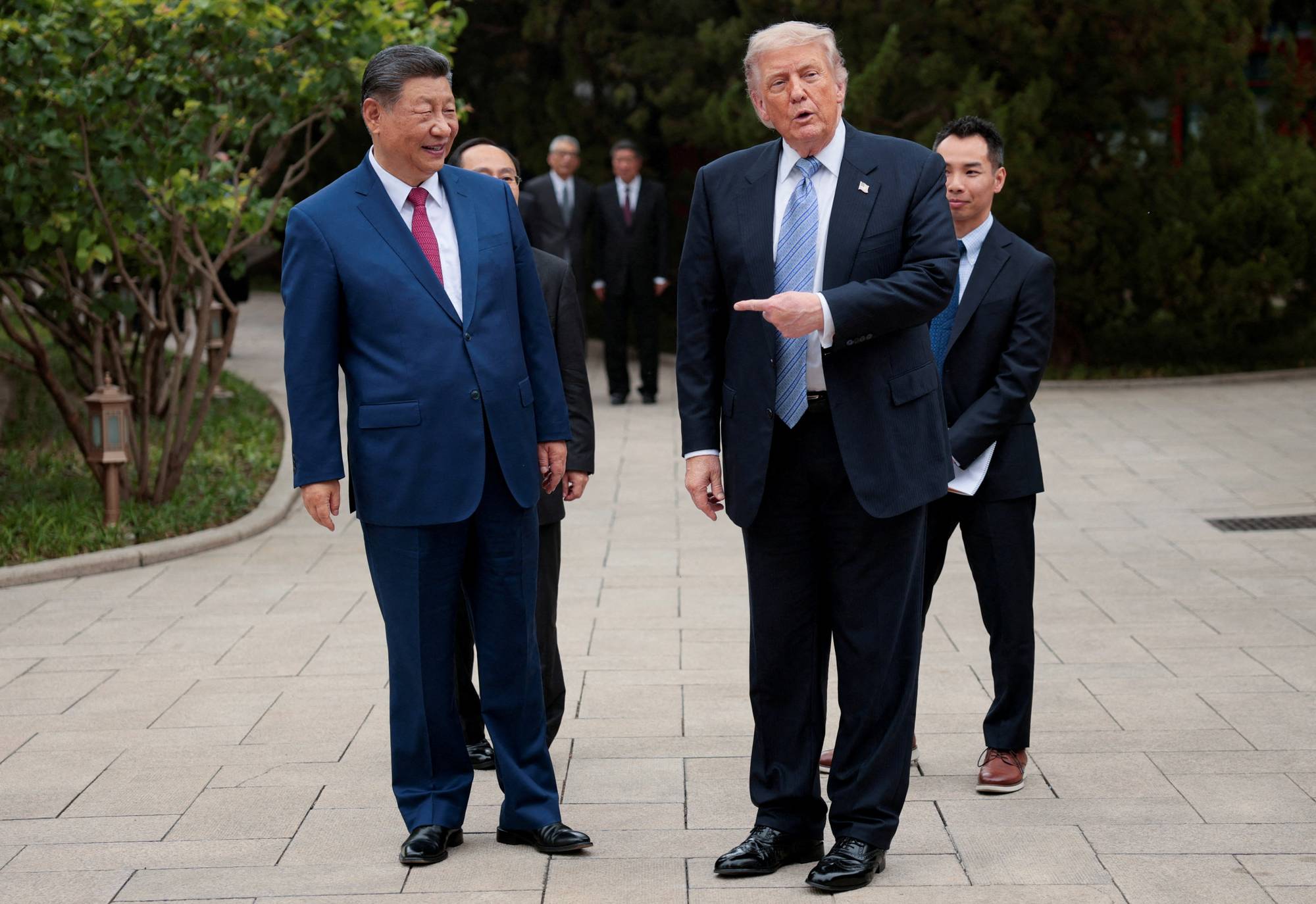 USAs president Donald Trump og Kinas president Xi Jinping under et møte. De står utendørs, flankert av andre menn. Trump peker mot venstre mens Xi ser mot Trump. (Bildebeskrivelsen er laget av en KI-tjeneste)