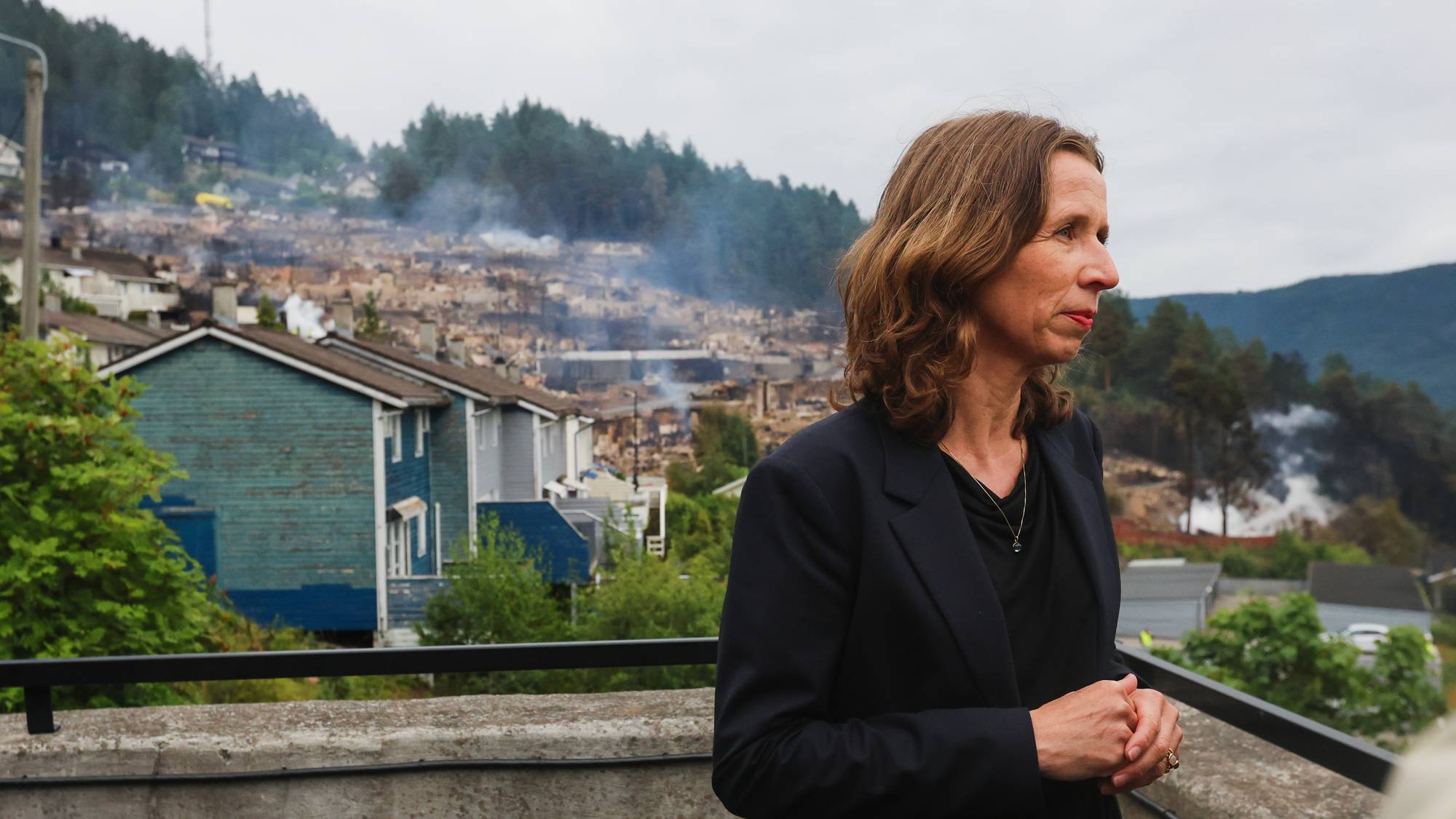 Kvinne ser utover et boligområde med brannskader og røyk. 