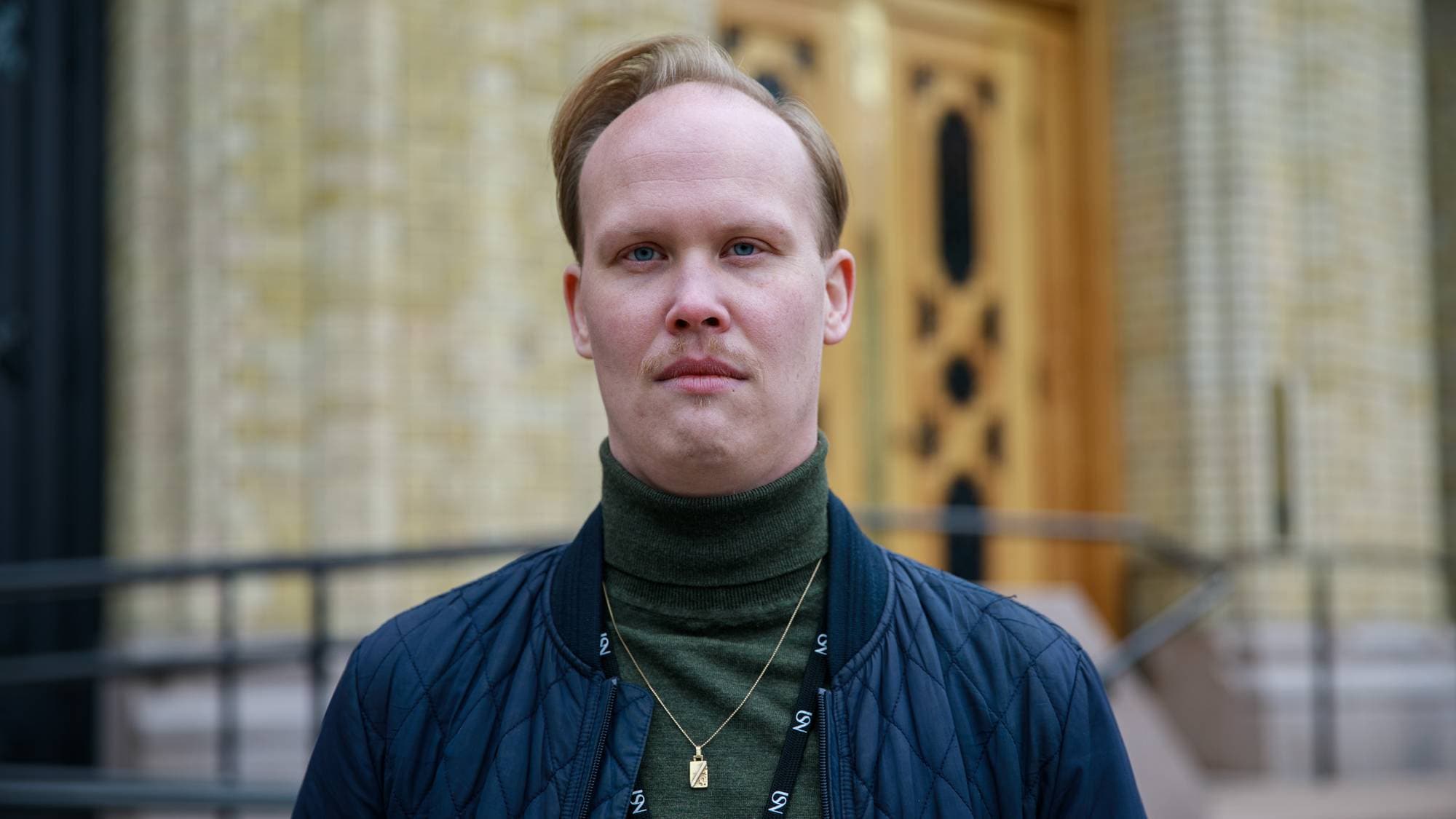 Frode Stenrud, iført blå jakke, ser strengt mot kameraet foran Stortinget. 